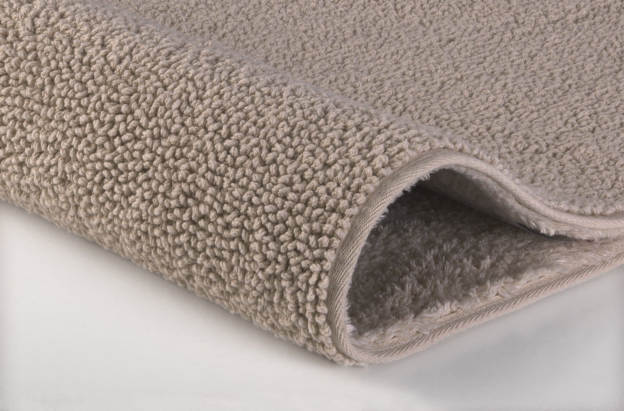 Badteppich CHRISSY Natur 55 x 65 cm liegt zusammengerollt und zeigt seine weiche, beigefarbene Oberfläche.