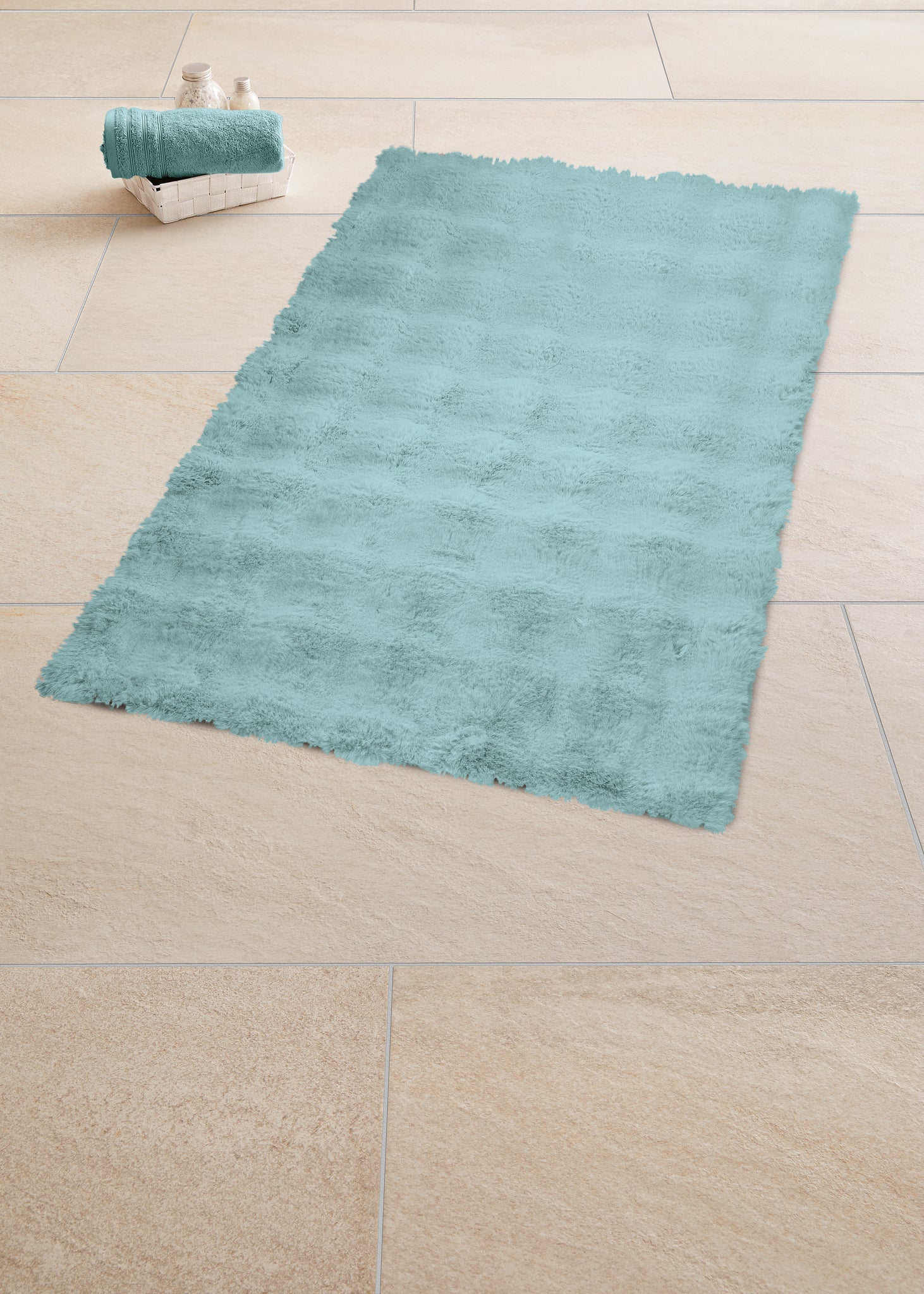 Badteppich CLOUD Opal 70 x 120 cm liegt auf hellen Fliesen neben Korb mit Handtüchern.