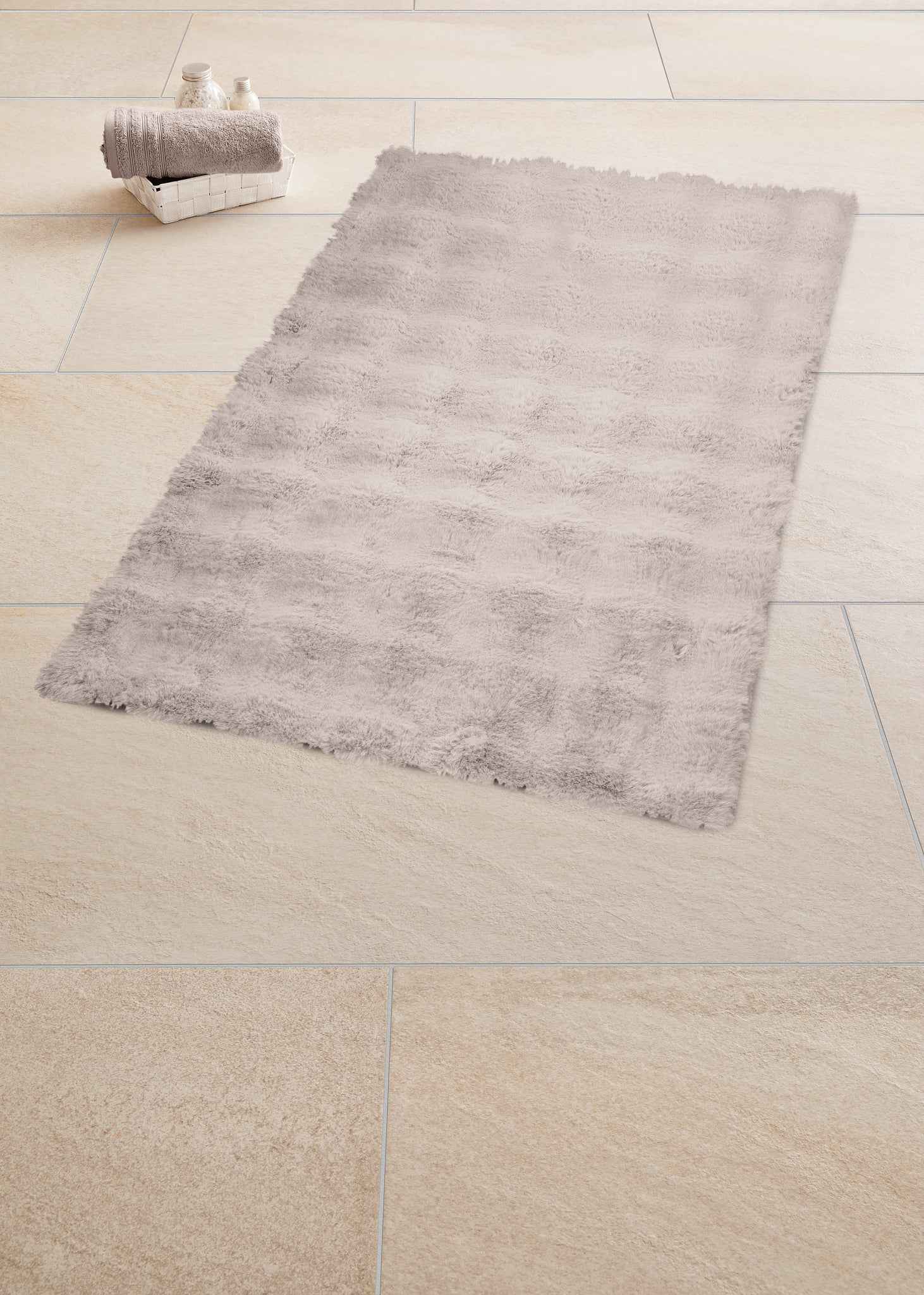 Badteppich CLOUD seidenfarben 70 x 120 cm liegt auf hellem Fliesenboden mit Handtüchern im Korb.