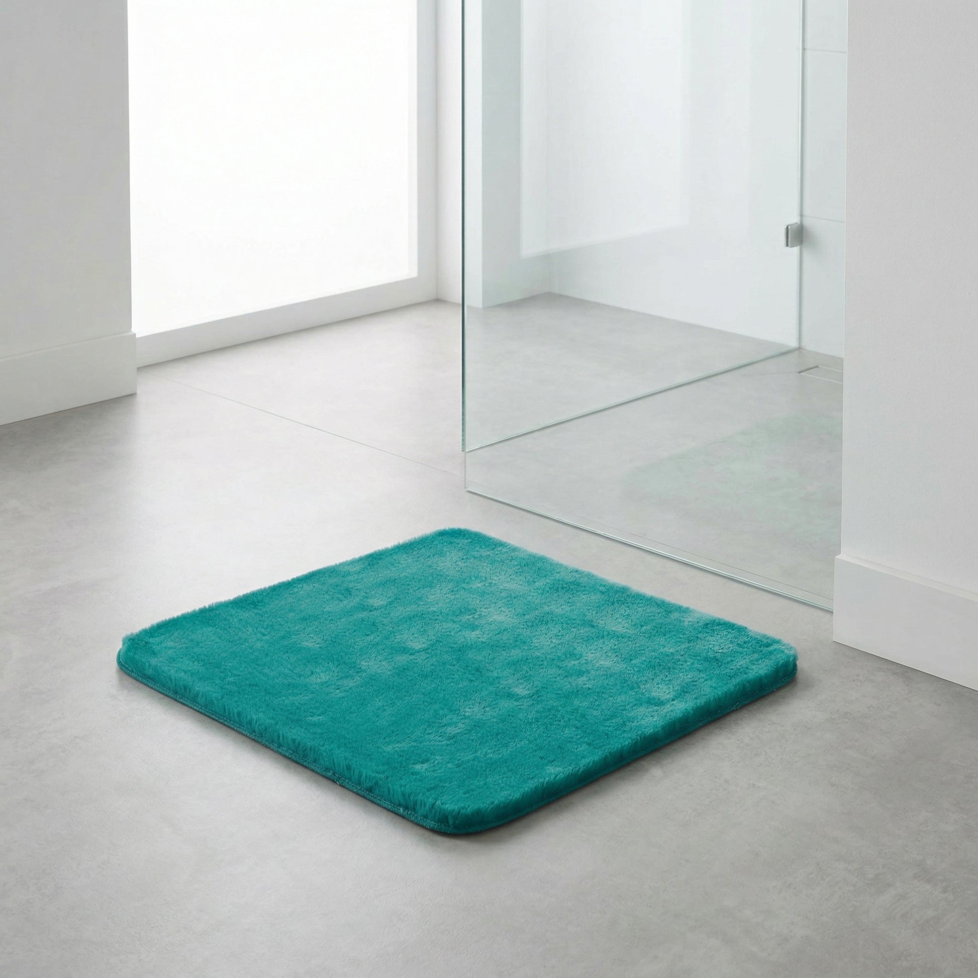 Türkise rechteckige Badematte vor Glasdusche im hellen modernen Bad