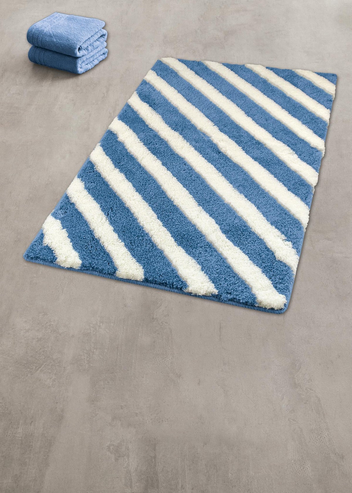 Blau-weißer Badteppich mit diagonalen Streifen, daneben zwei Handtücher.