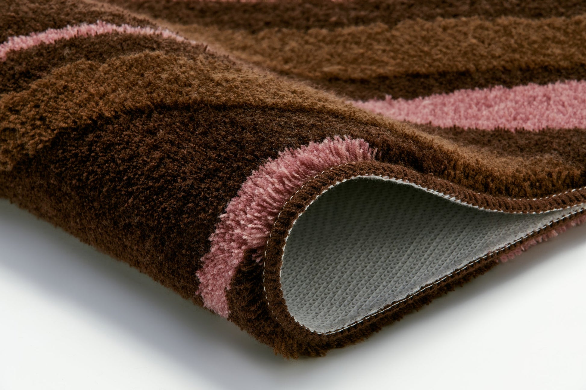 Nahaufnahme braun-rosa gestreifter Badteppich, leicht eingerollte Ecke