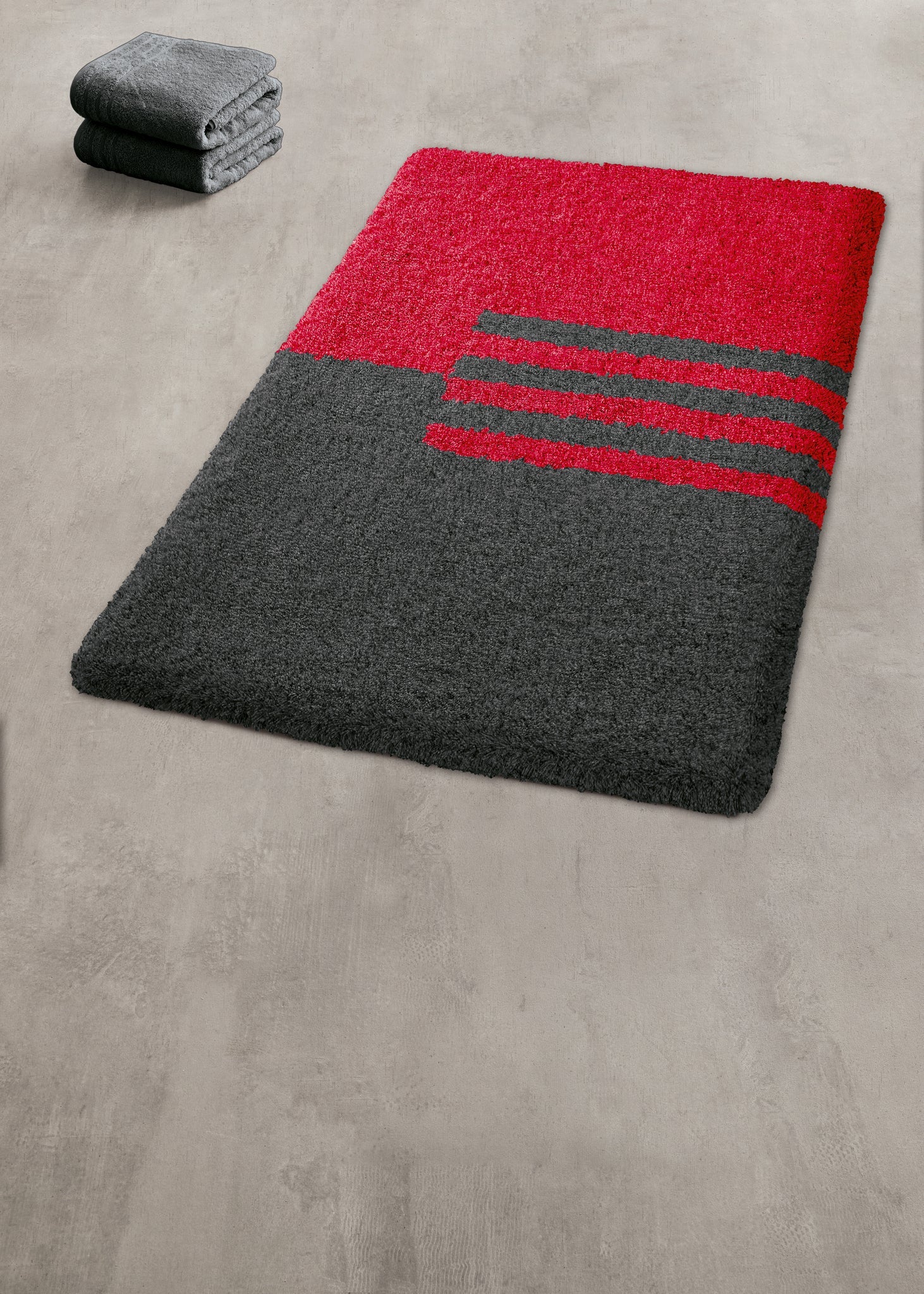 Badteppich DYNAMIC Rubin 70 x 120 cm liegt rot-grau gemustert auf hellem Badezimmerboden.
