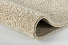 Nahaufnahme eines beigen, flauschigen Badteppichs mit umgeschlagener Kante