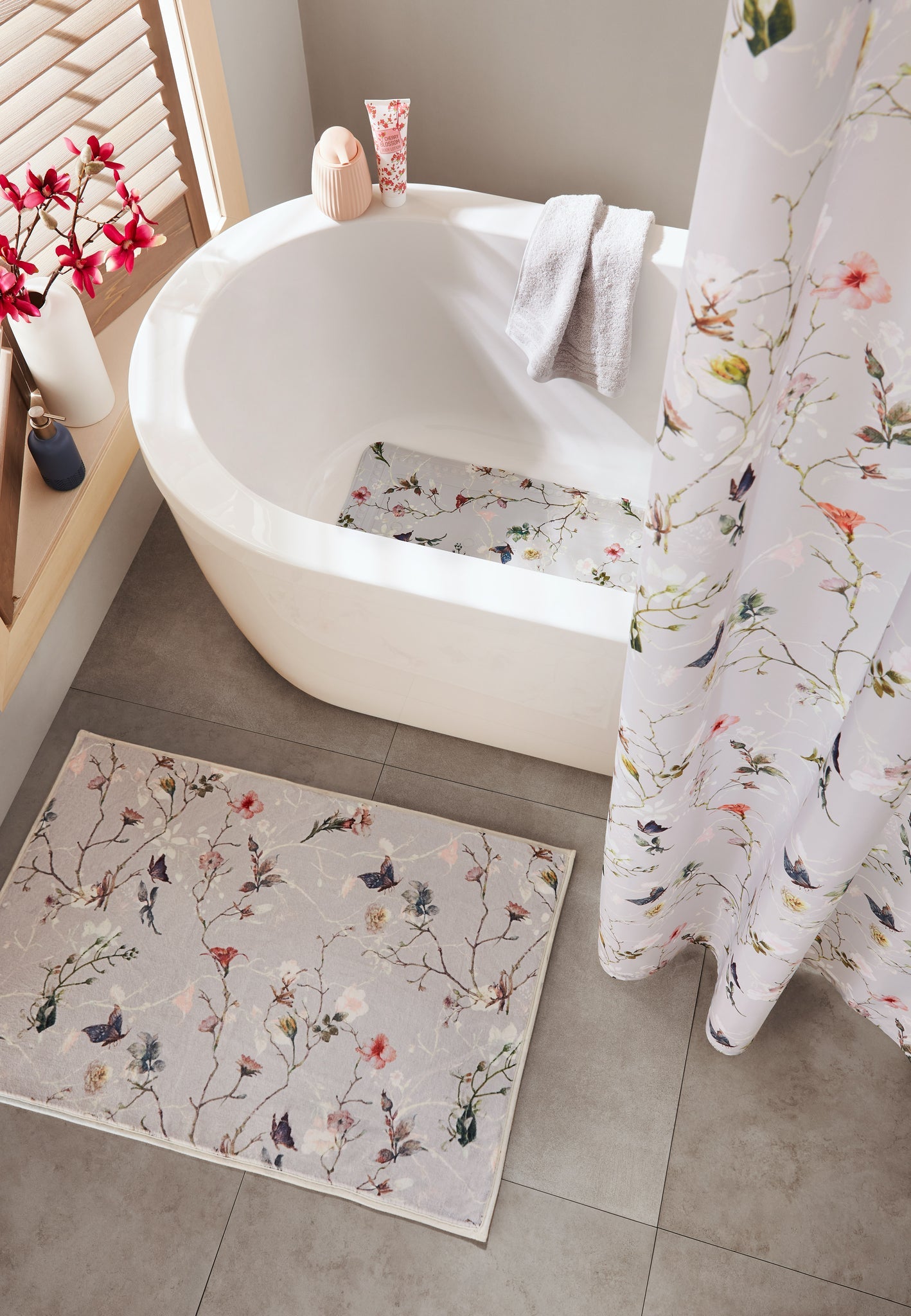 Badteppich FLORES Multicolor 60 x 90 cm liegt vor weißer Badewanne mit passendem Duschvorhang.