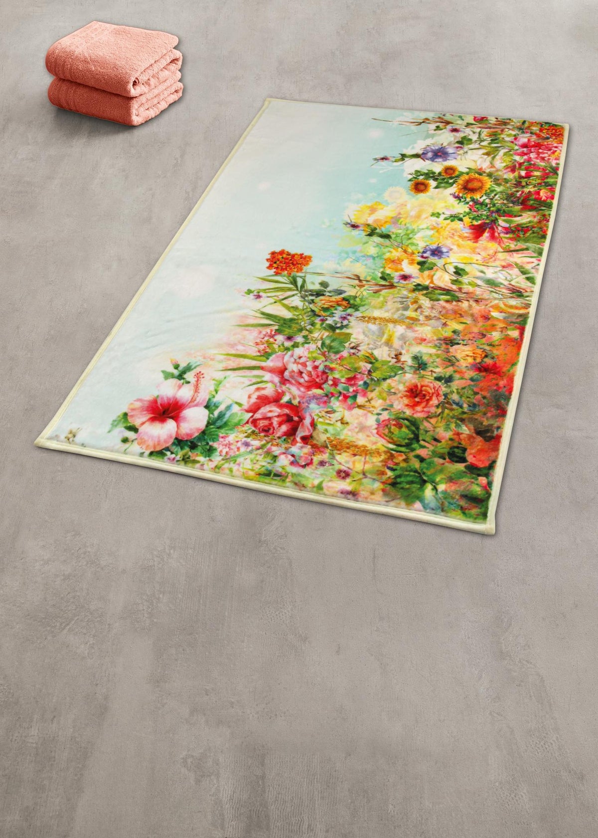 Badteppich mit buntem Blumenmotiv auf grauem Boden neben rosa Handtüchern.