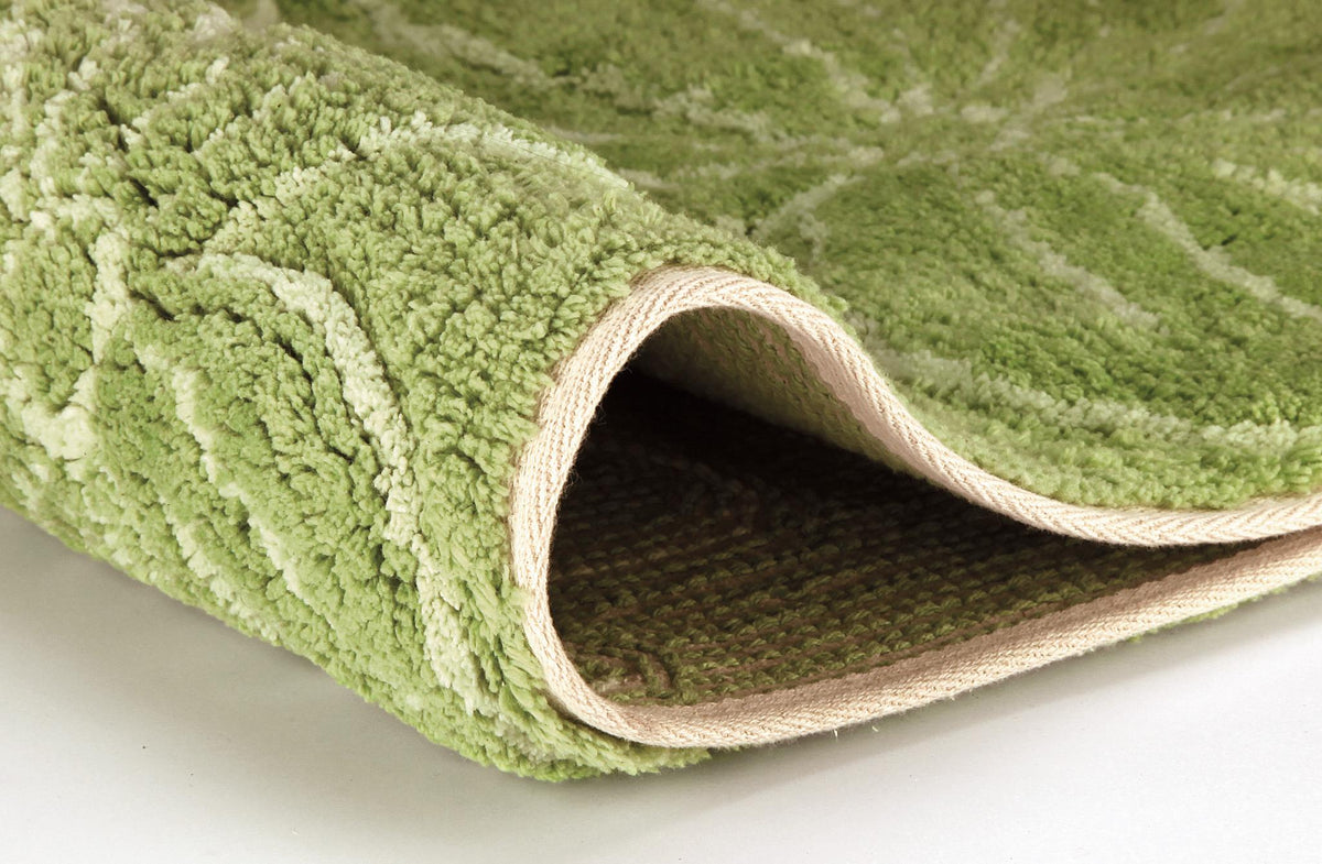 Aufgerollter grüner Hochflor-Teppich mit hellem Muster im Detail.