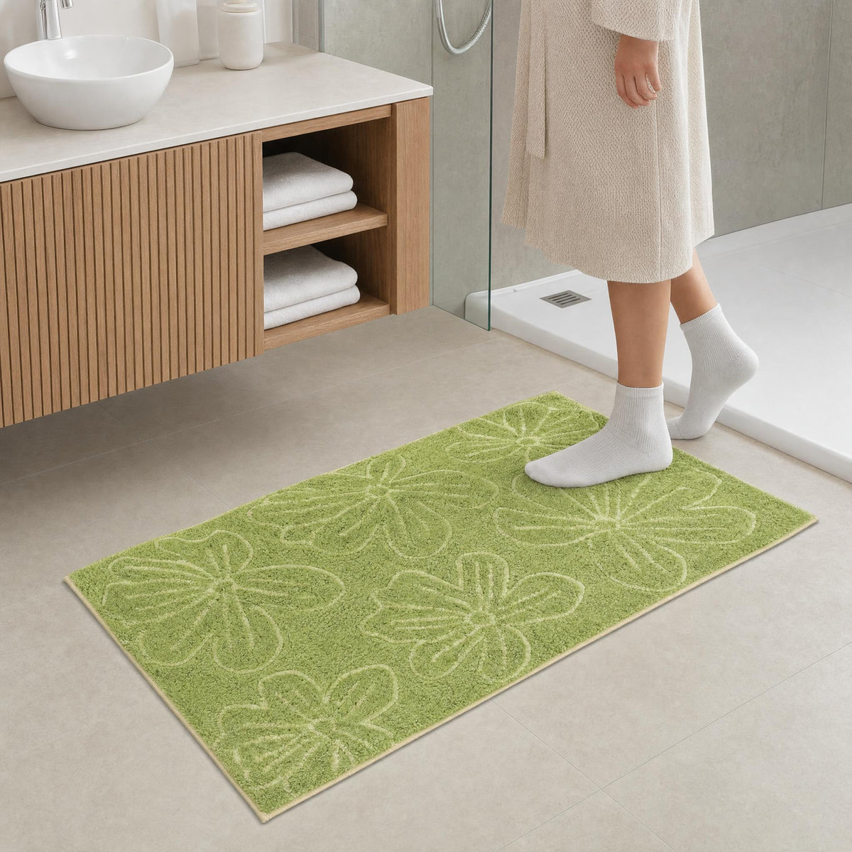 Grüne Badematte mit Blumenmuster vor Waschtisch und Dusche im Bad.
