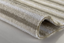 Nahaufnahme eines gefalteten, beige-weiß gestreiften Badteppichs