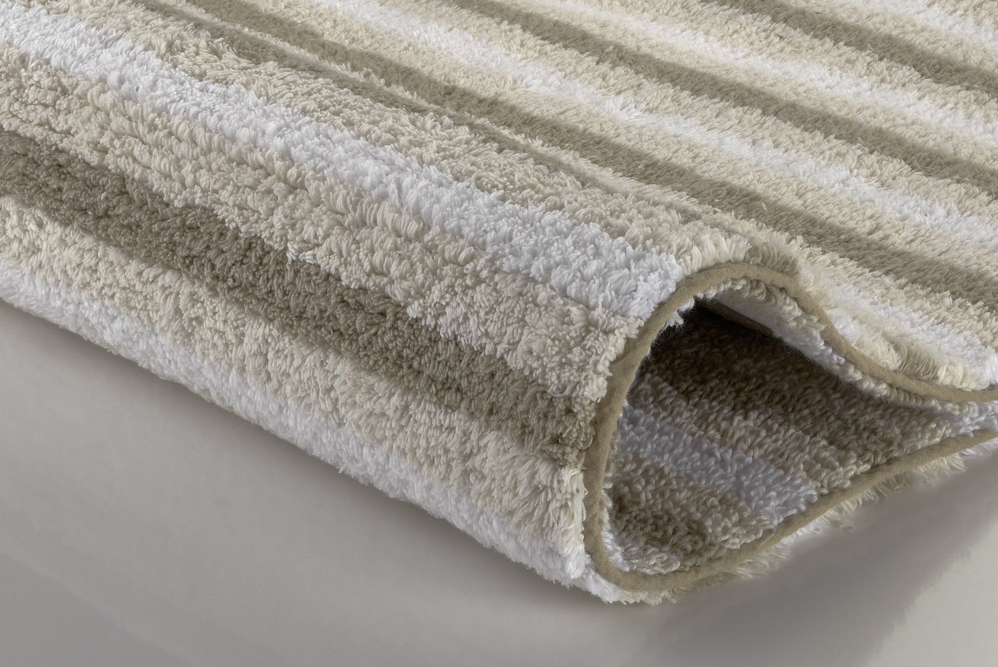 Nahaufnahme eines gefalteten, beige-weiß gestreiften Badteppichs