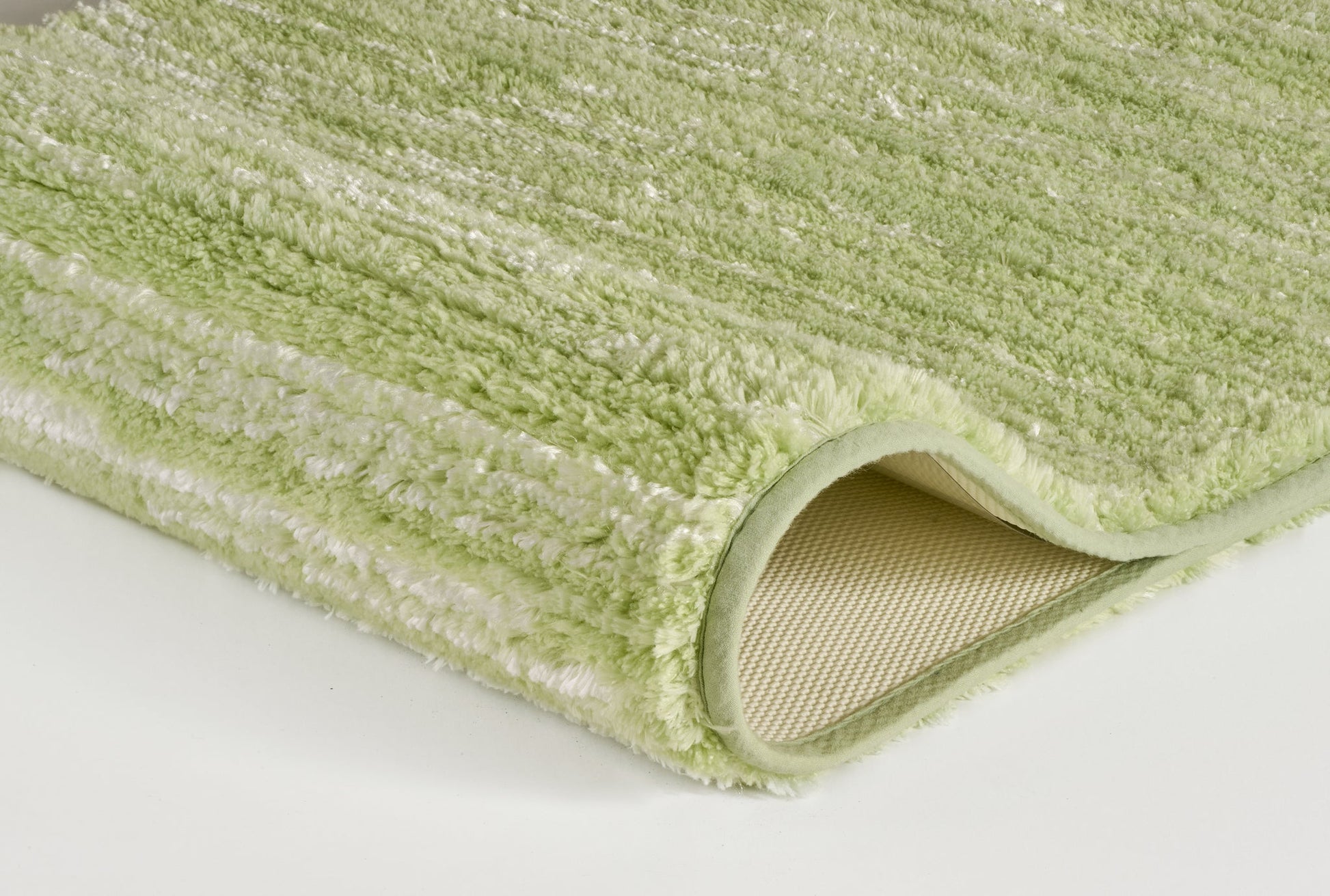Hellgrüner, flauschiger Badteppich mit gerollter Ecke unten auf Weiß