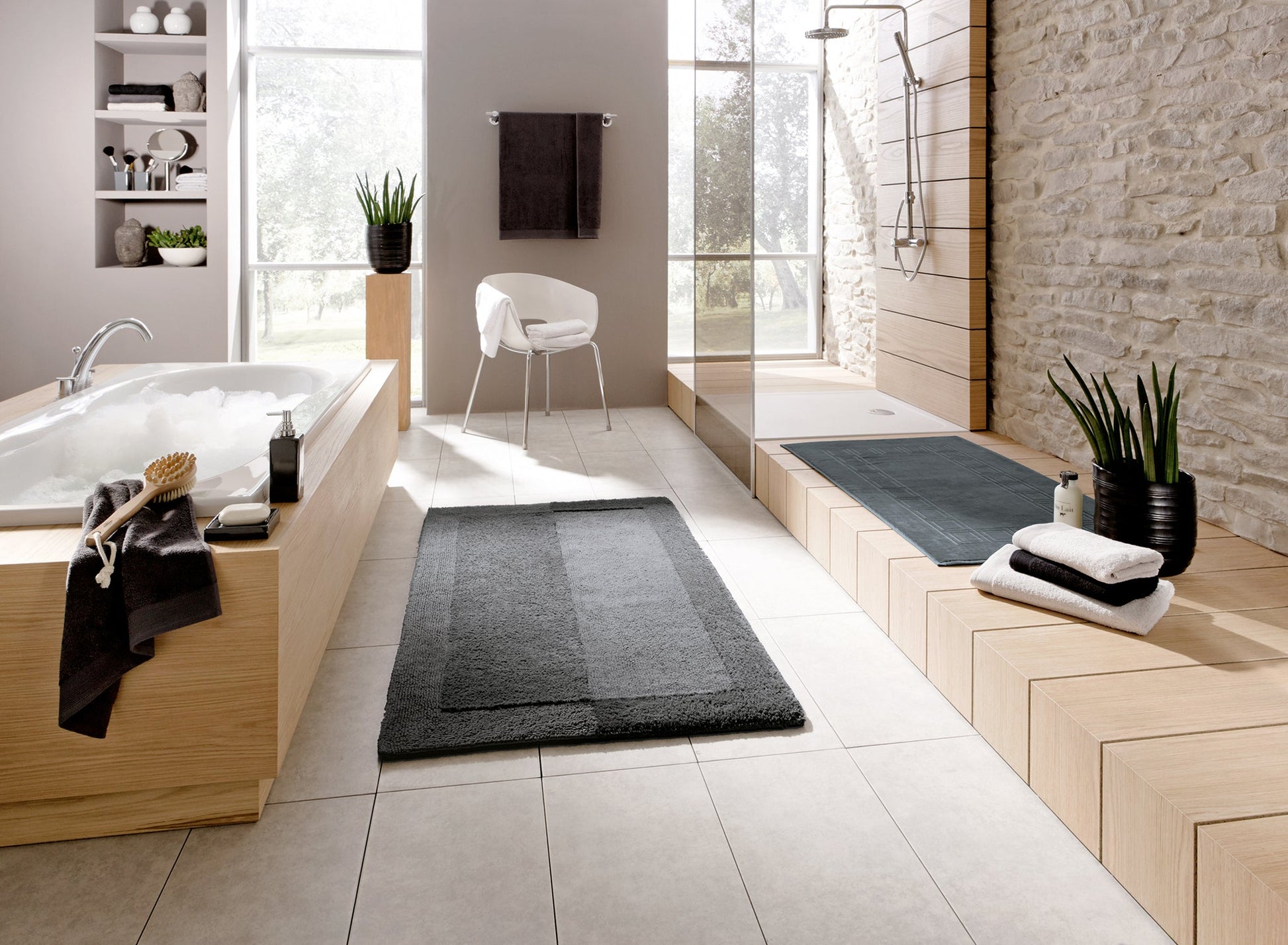 Modernes Bad mit Wanne, Dusche, grauen Badematten und Handtüchern