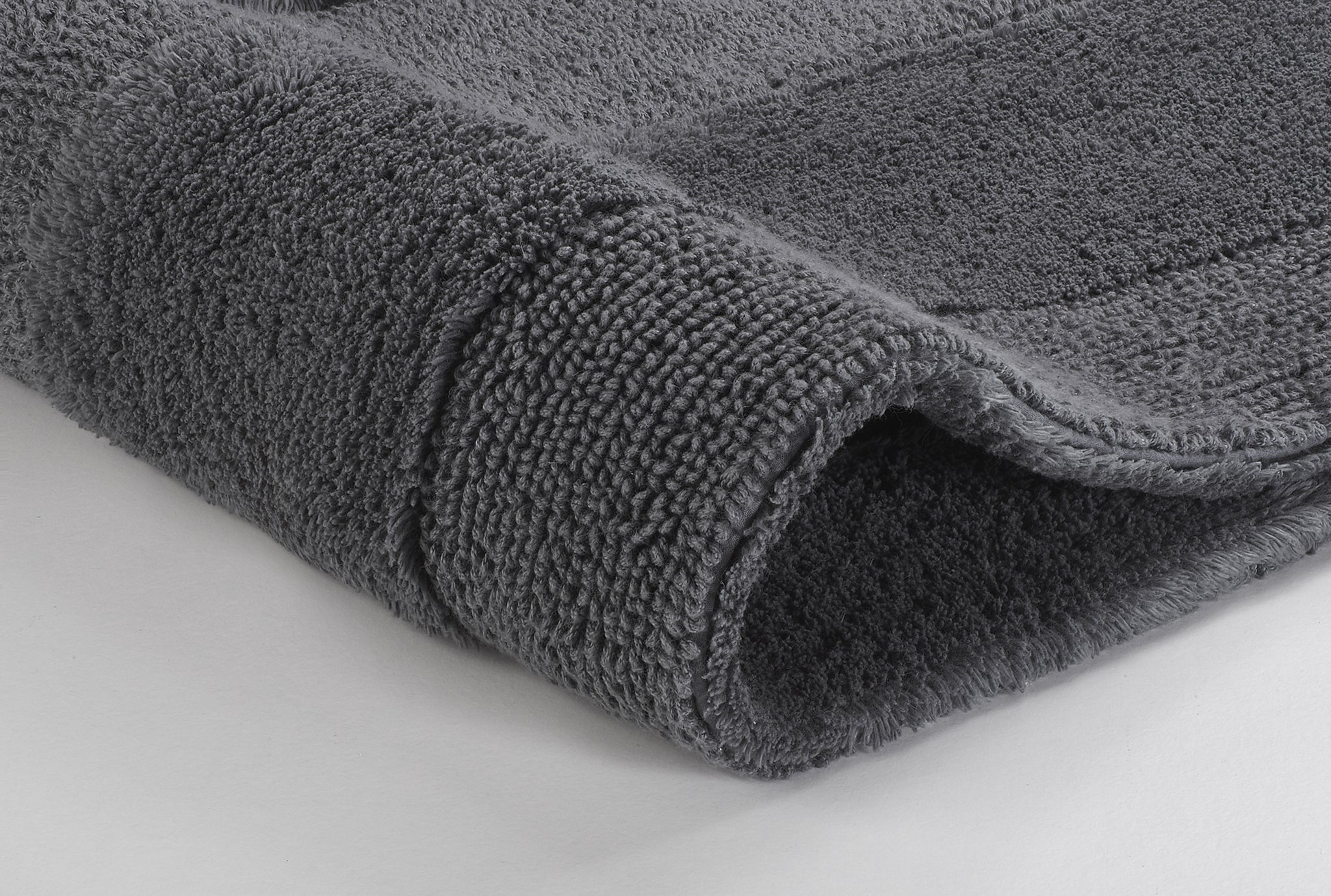 Graue, flauschige Badematte in Detailansicht auf hellem Untergrund