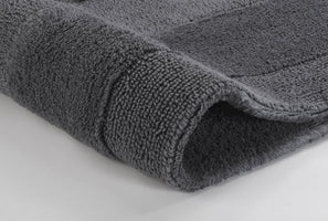 Nahaufnahme einer grauen, flauschigen Badematte mit umgeschlagener Ecke