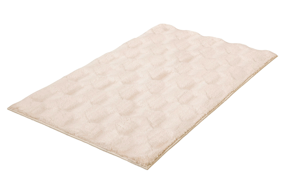 Cremefarbiger, flauschiger Badteppich auf weißem Grund.