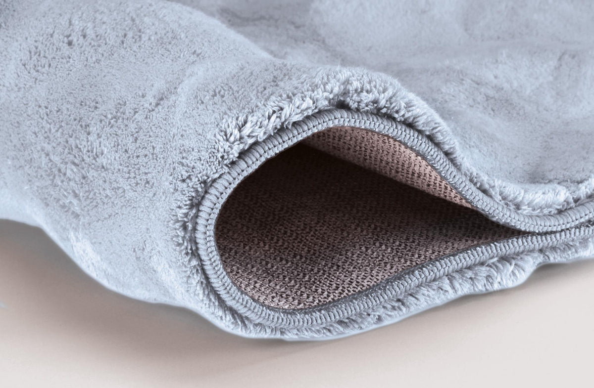 Hellblauer, flauschiger Badteppich mit umgeschlagener Ecke und Wabenoptik.