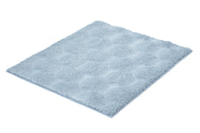 Hellblauer flauschiger Badteppich mit Wabenmuster auf Weiß.