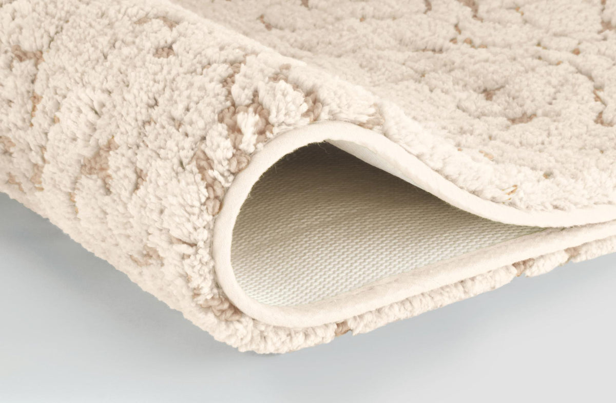 Zusammengerollter cremefarbener Badteppich mit weicher, flauschiger Struktur.