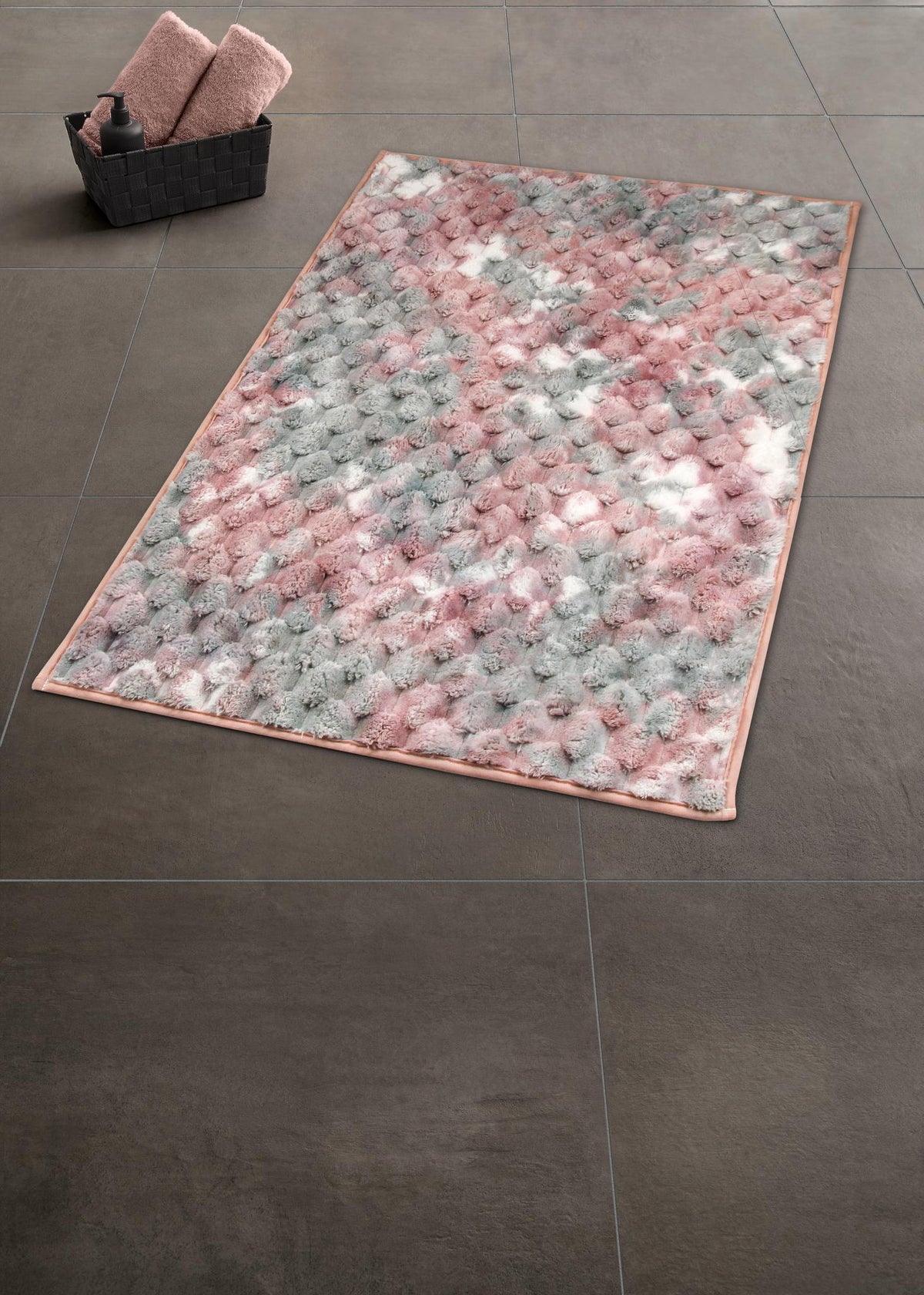 Flauschige Badematte in Rosa, Grau und Weiß auf dunklem Fliesenboden.