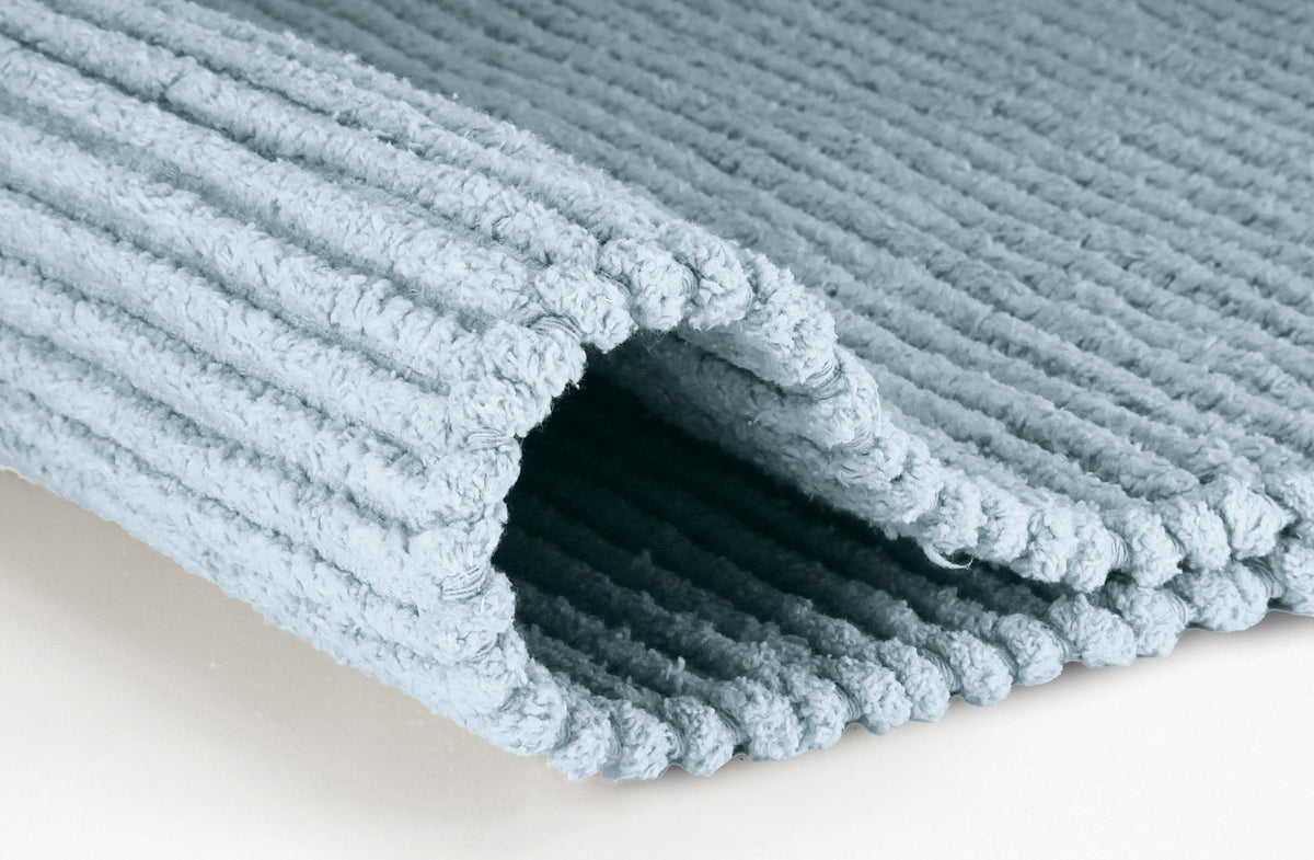 Hellblauer gerippter Badteppich, teilweise umgeschlagen.