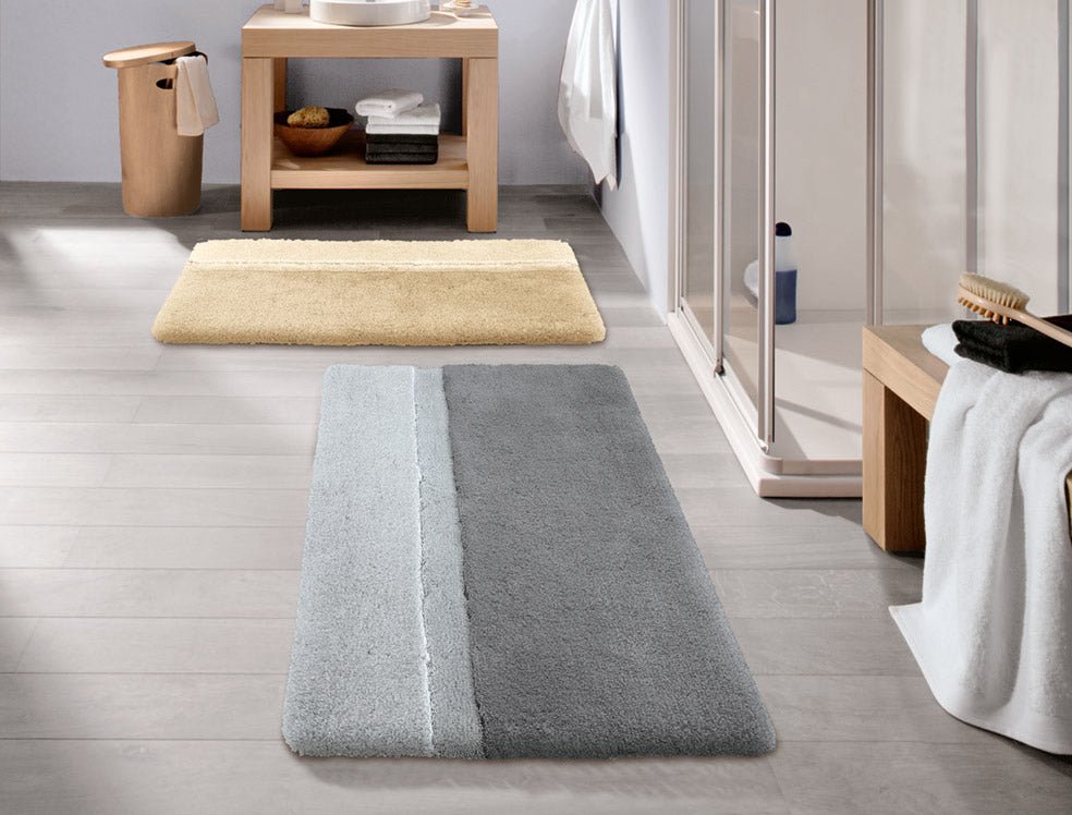 Grauer und beiger Badezimmerteppich auf hellem Fliesenboden nebeneinander