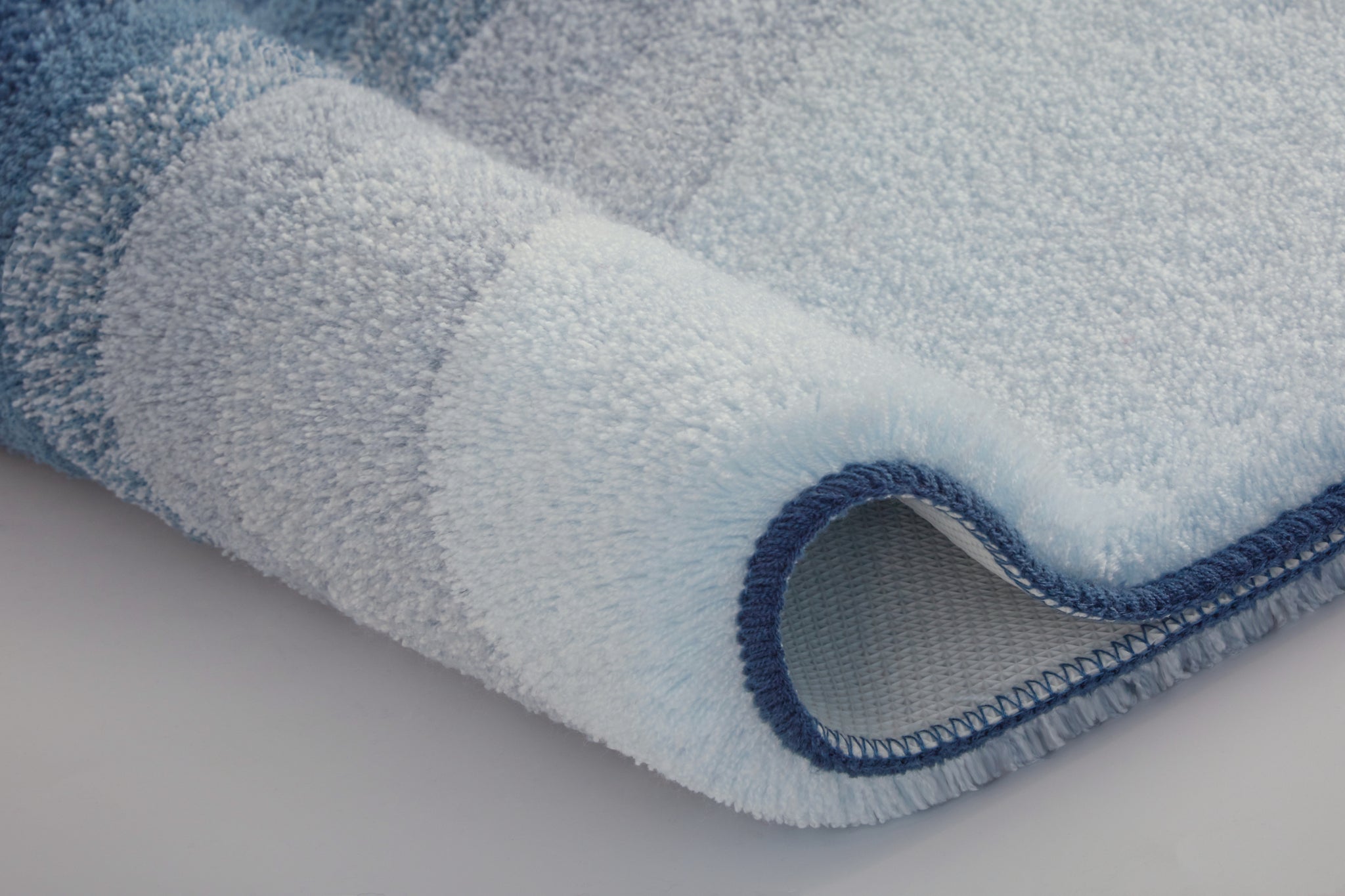 Nahaufnahme einer blau gestreiften Badezimmermatte mit gerollter Kante