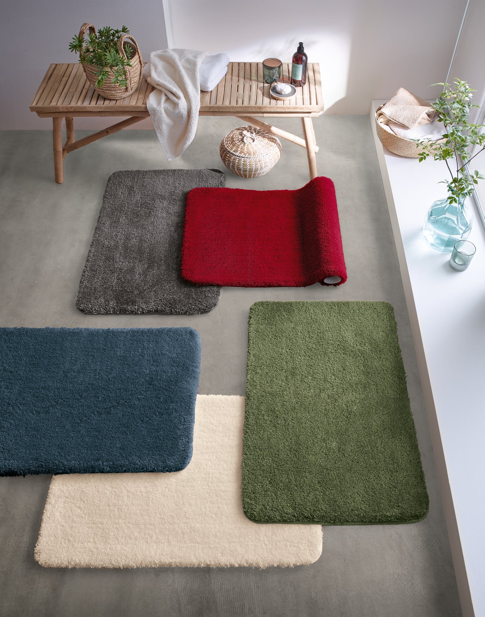 Badteppich MARCO Granat 50 x 60 cm liegt im Bad neben weiteren farbigen Badteppichen und Accessoires.