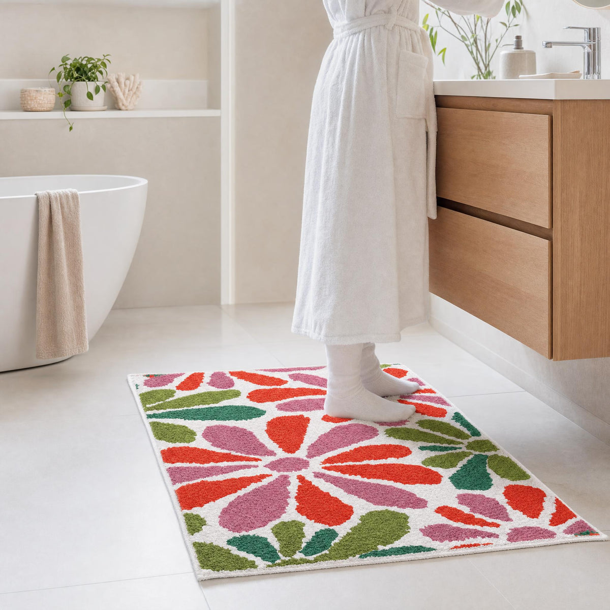 Person im Bademantel auf floralem Badteppich im hellen Badezimmer.