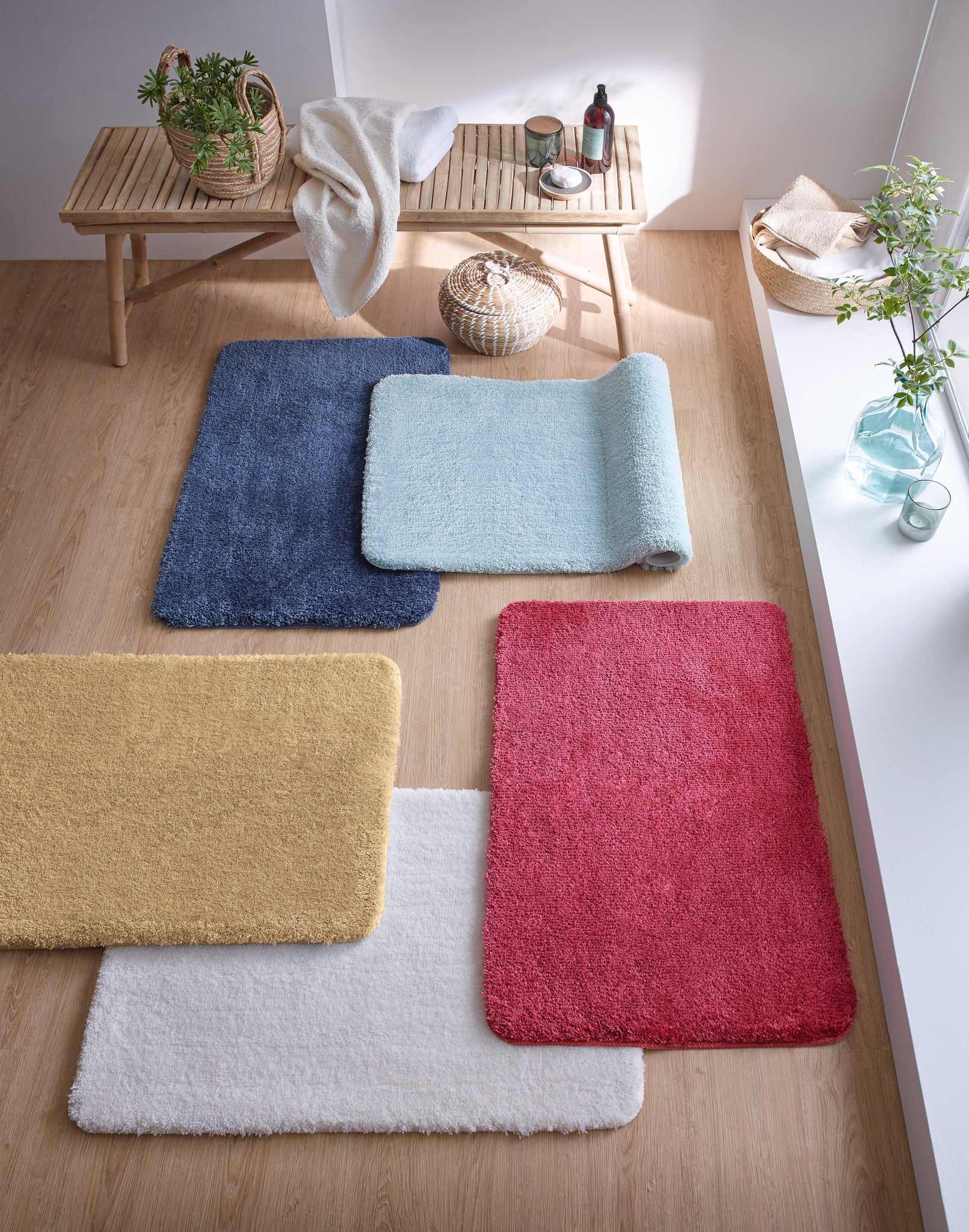 Fünf farbige Badteppiche auf Holzfußboden neben Bank und kleinen Pflanzen