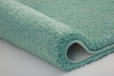 Türkisgrüne, flauschige Badematte in Nahaufnahme mit leicht gerollter Kante