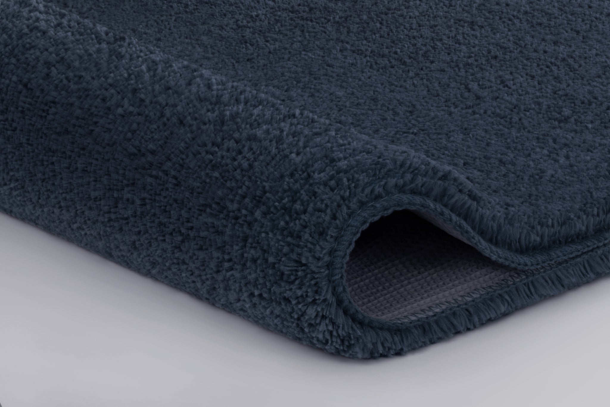 Nahaufnahme dunkelblauer, weicher Badteppich mit leicht gerollter Kante