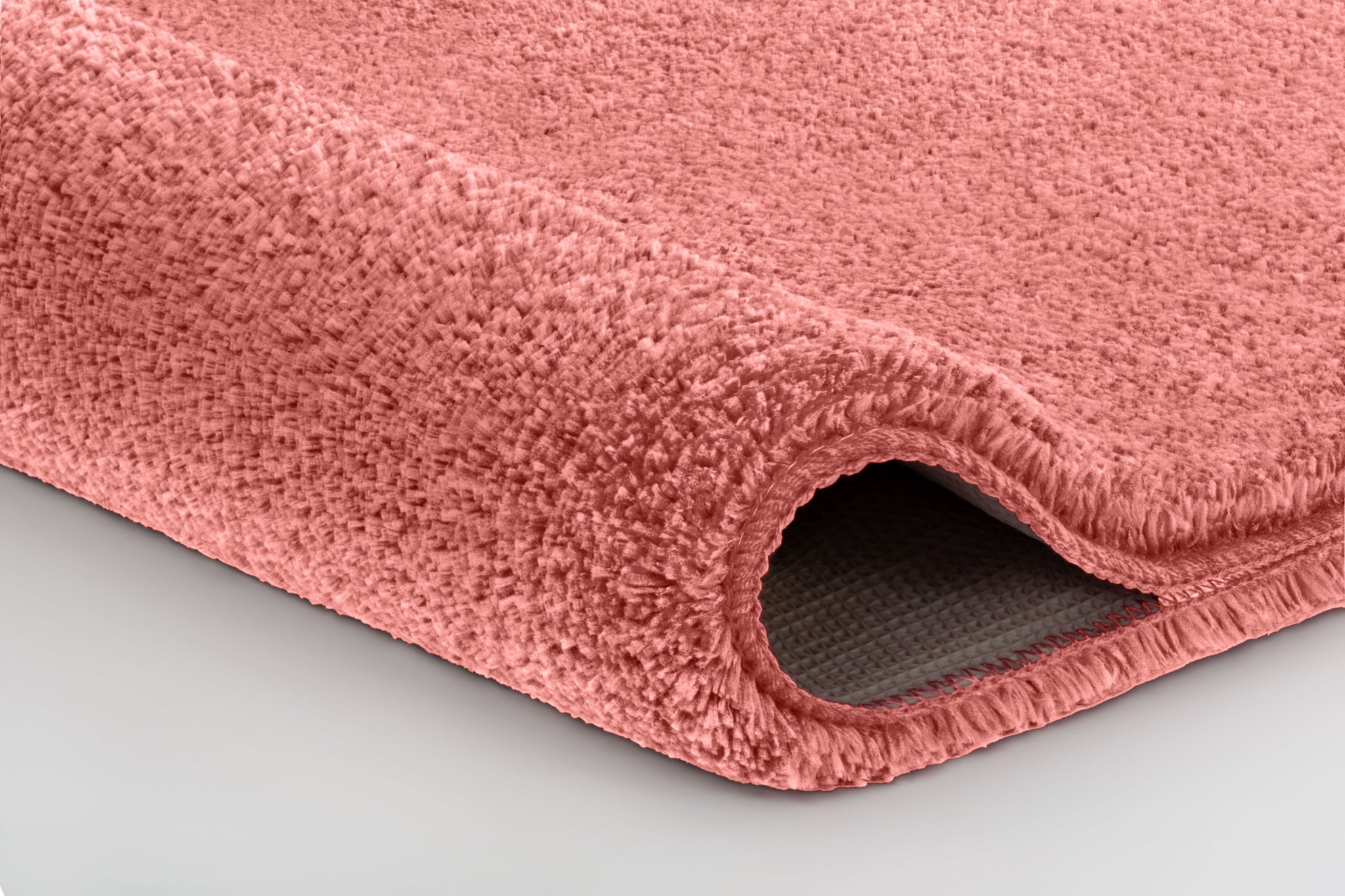 Detailaufnahme einer rosafarbenen Badematte mit abgerundeter Kante