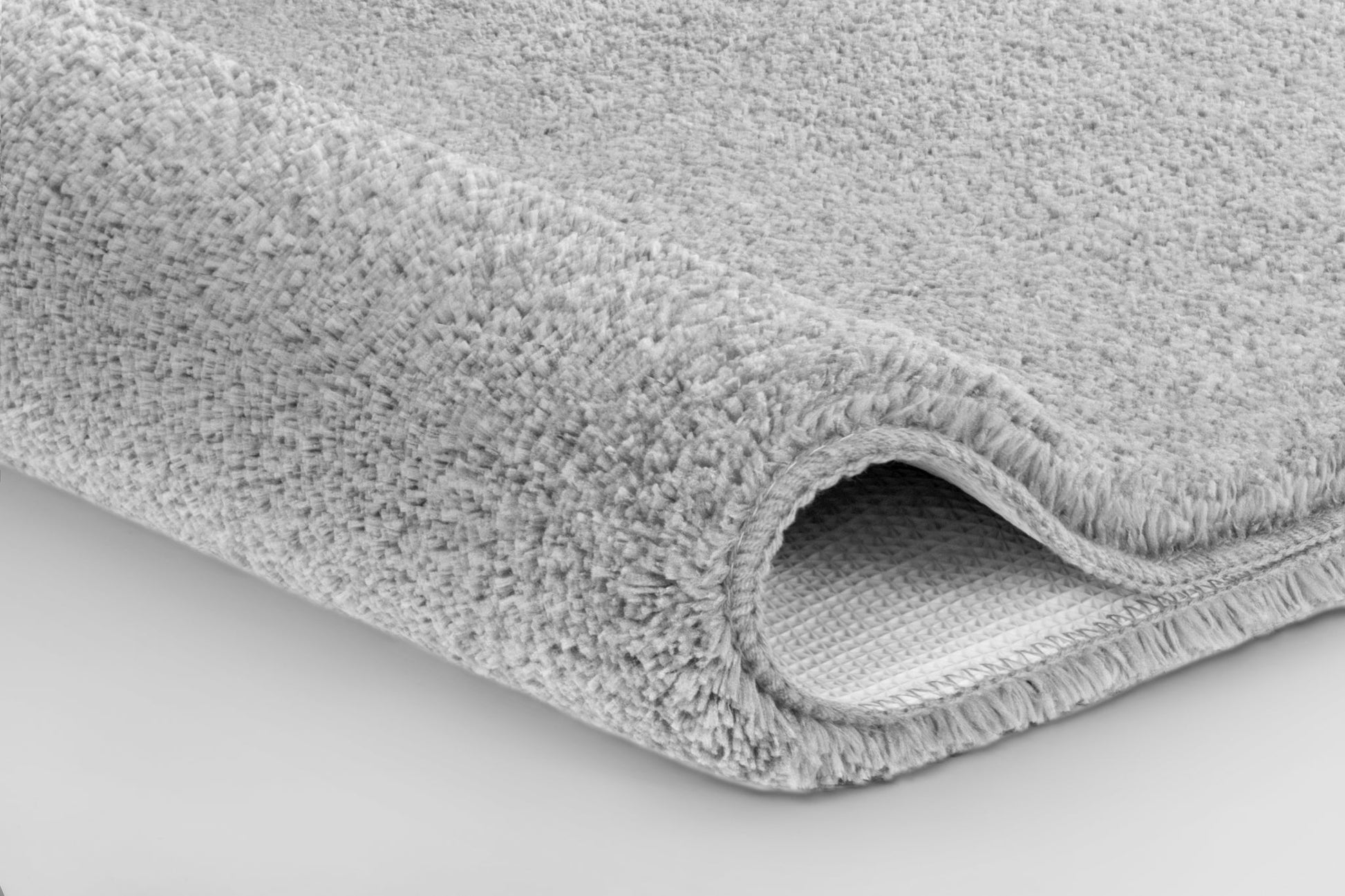 Nahaufnahme einer hellgrauen, flauschigen Badematte auf hellem Boden