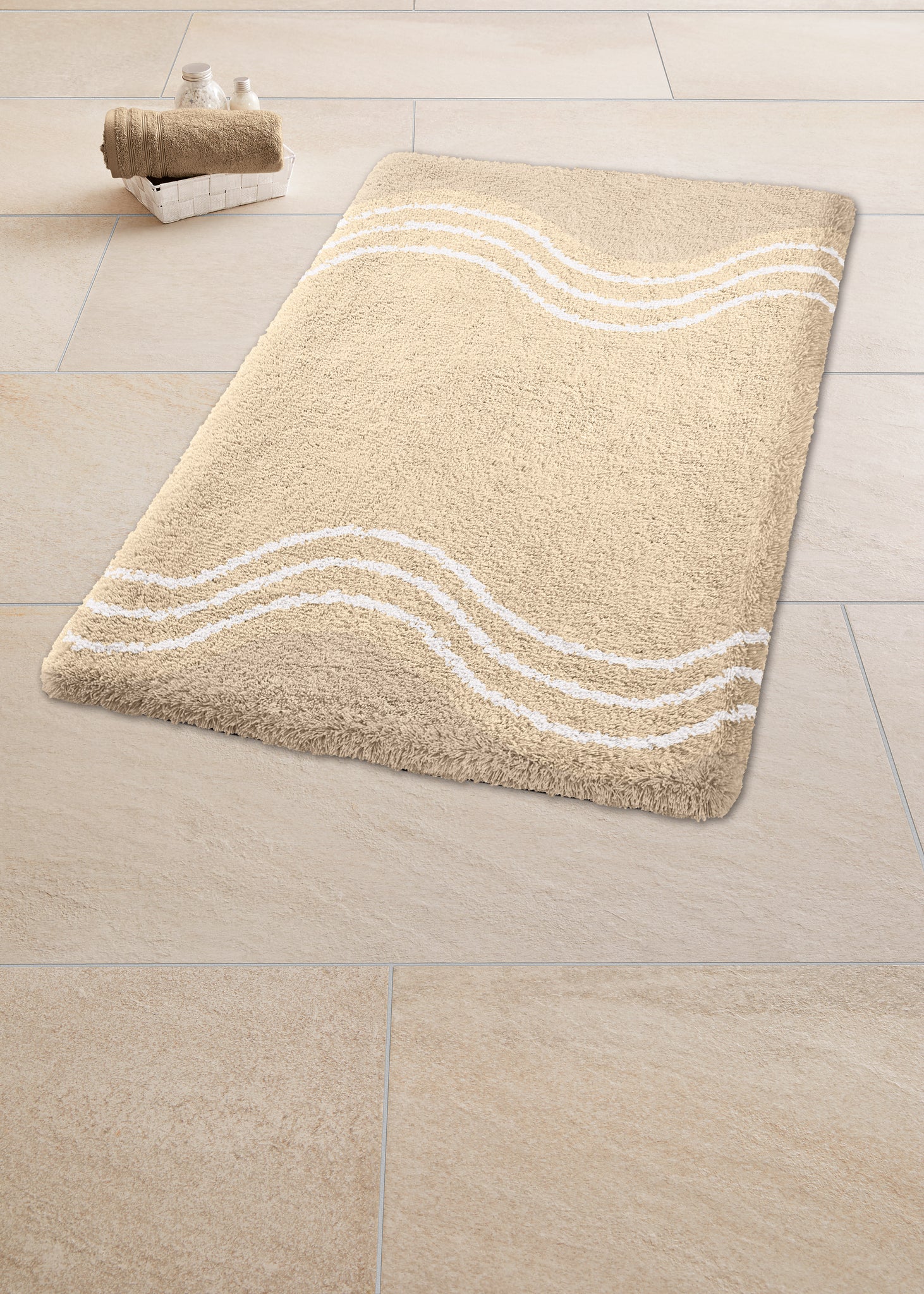 Sandbeiger Badteppich MOVE 65 x 115 cm mit weißen Wellenlinien liegt auf hellen Badezimmerfliesen.