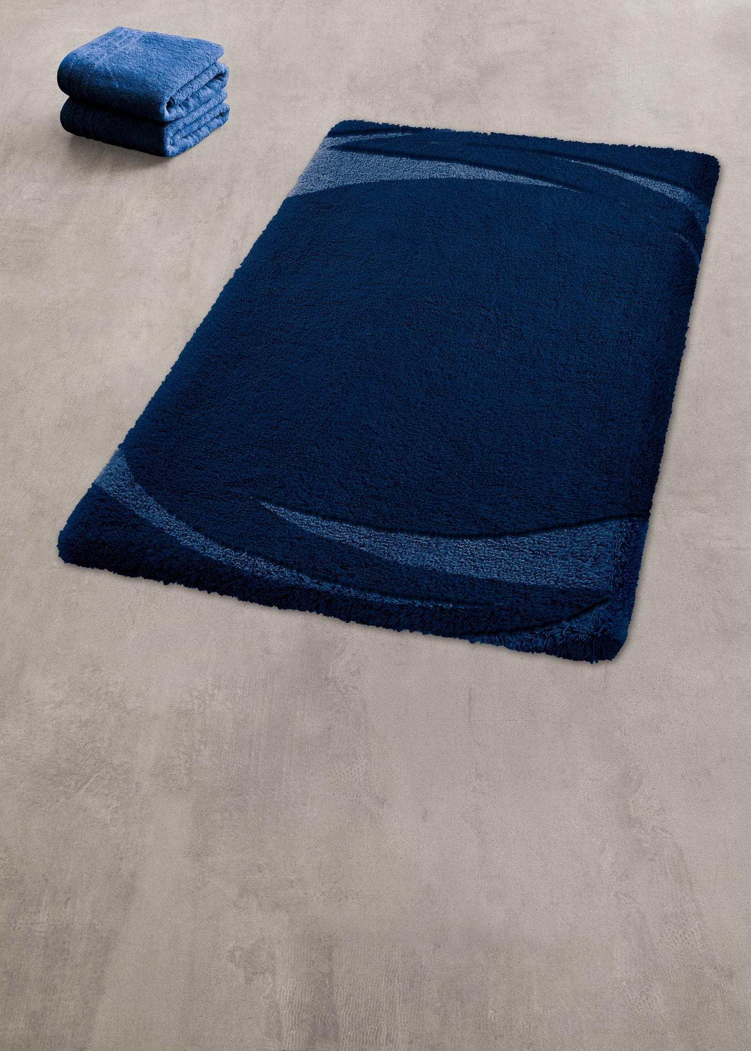Badteppich MYSTIC Navy mit Handtüchern auf hellem Badezimmerboden.