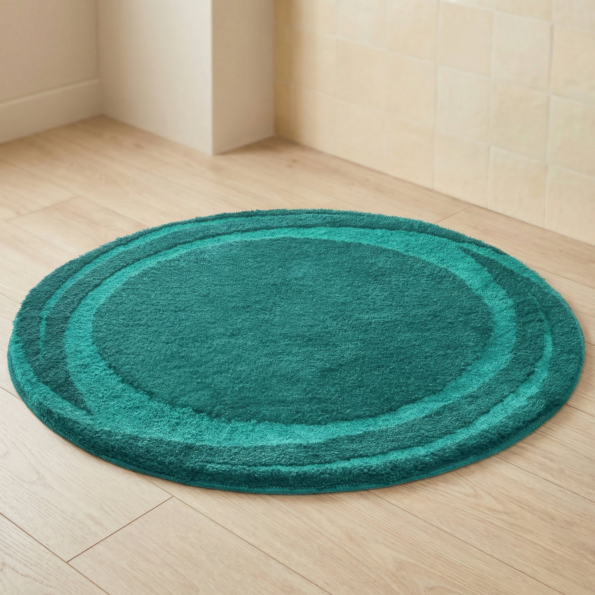 Runder türkisgrüner Badteppich auf hellem Holzboden vor Fliesenwand