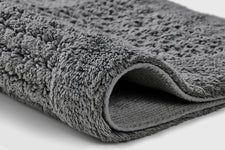 Graue, flauschige Badematte aus Textil im Detail in Nahaufnahme gezeigt