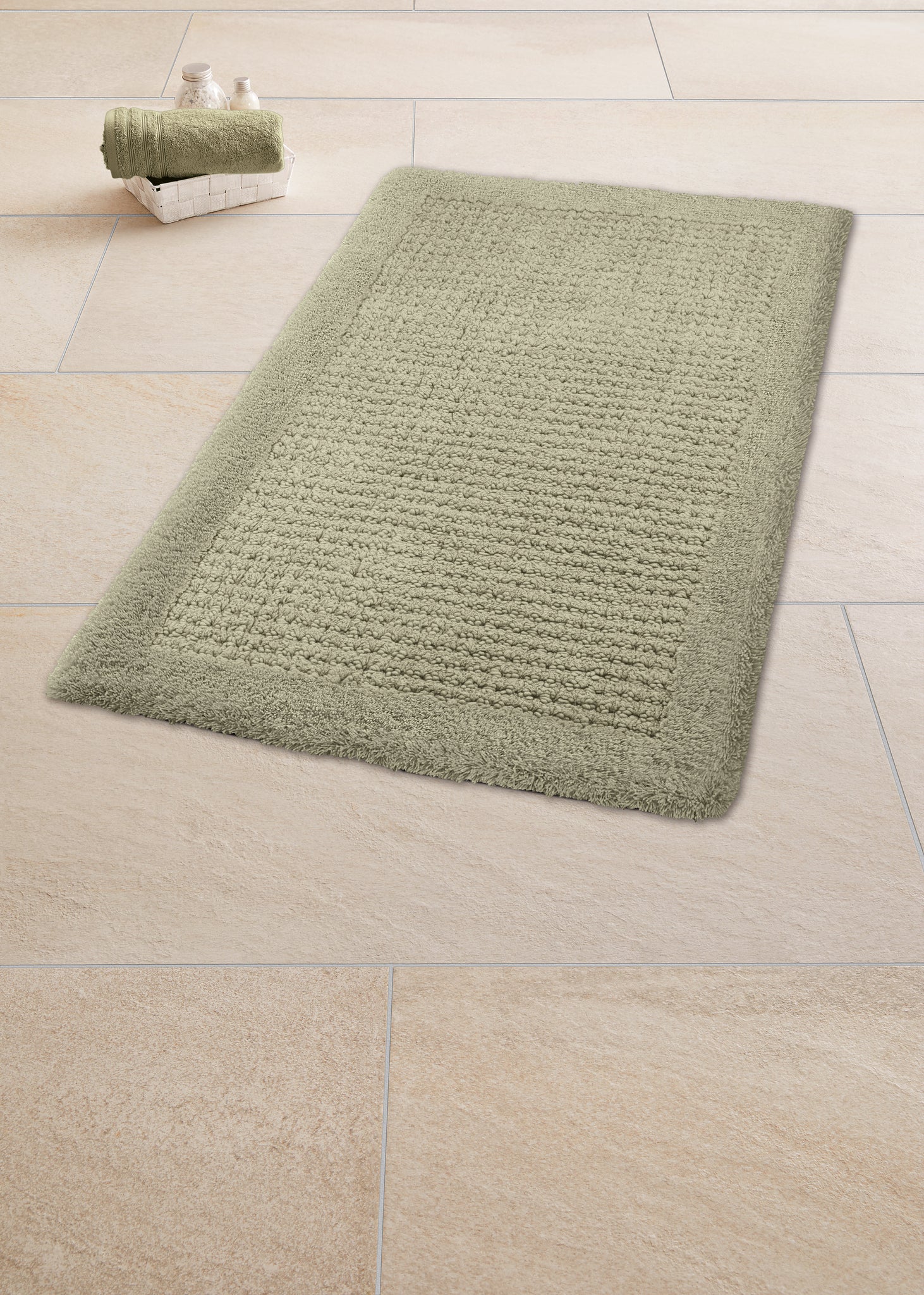 Badteppich NET Schilf 60 x 60 cm liegt auf hellen Fliesen neben gerolltem Handtuch im Korb.