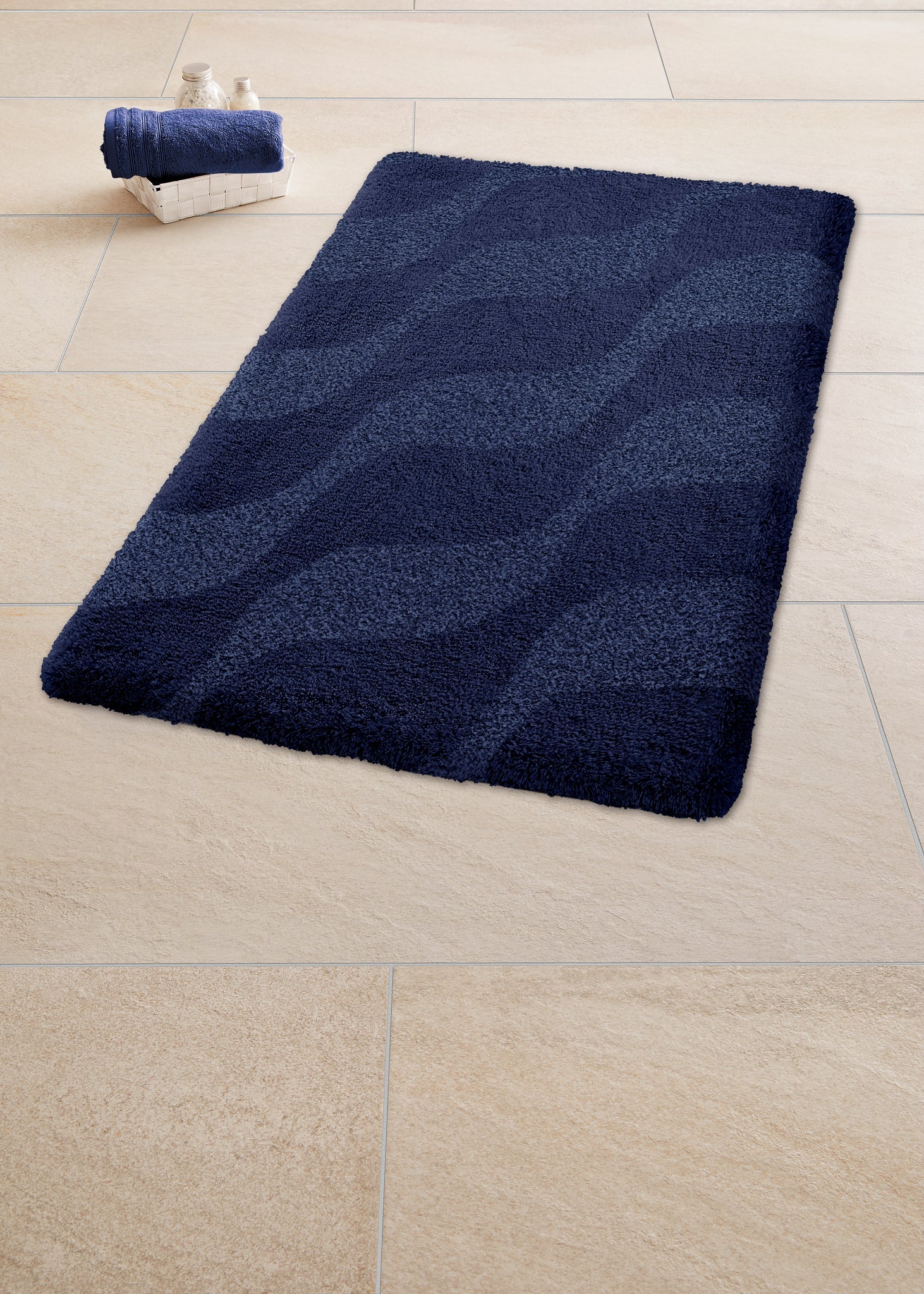 Badteppich ONDA Navy 60 x 90 cm liegt auf hellen Fliesen im Bad.