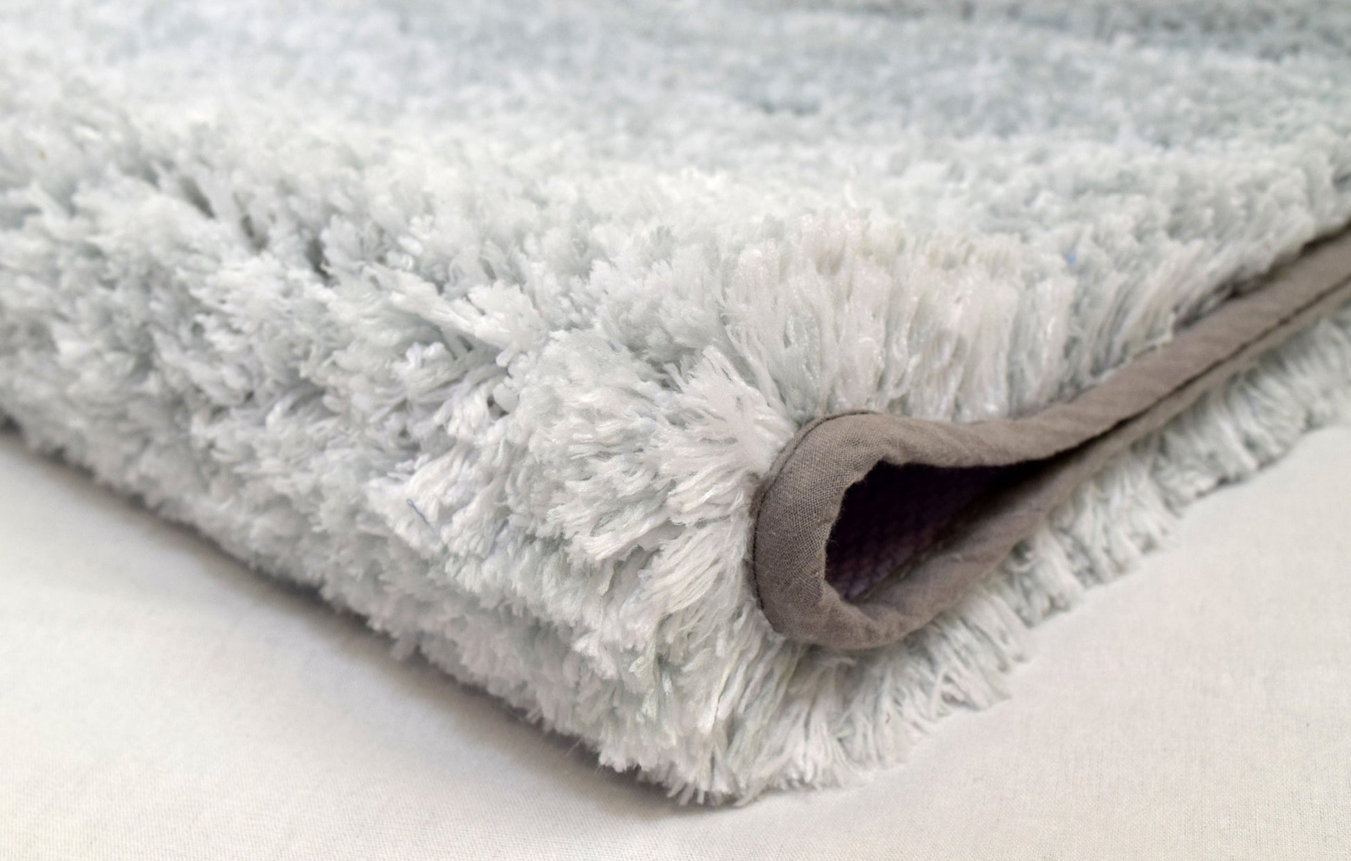 Gefaltete, graue, weiche, hochflorige Badematte in seitlicher Nahaufnahme