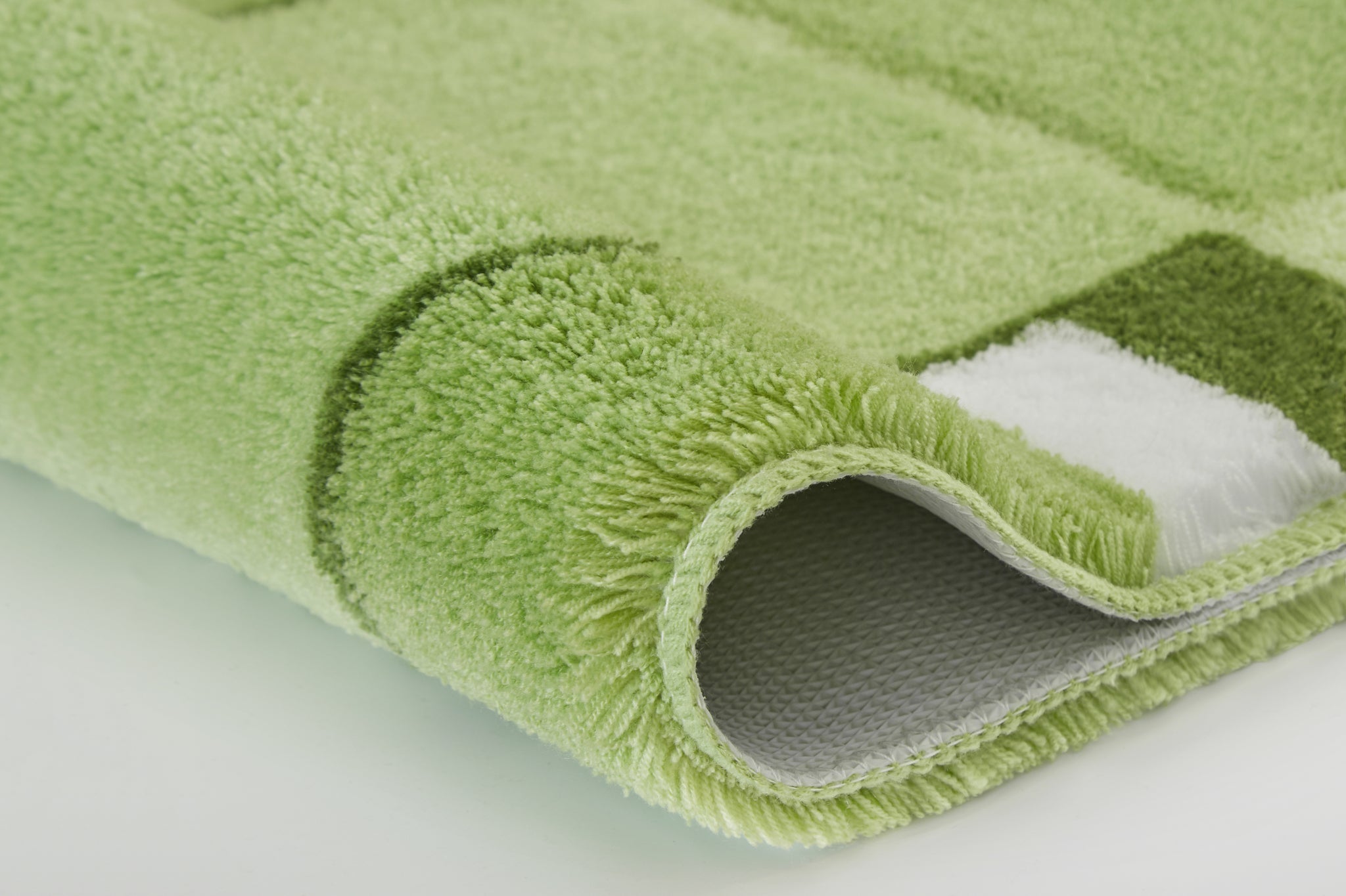 Nahaufnahme einer grünen Badematte mit Muster und gerollter Kante