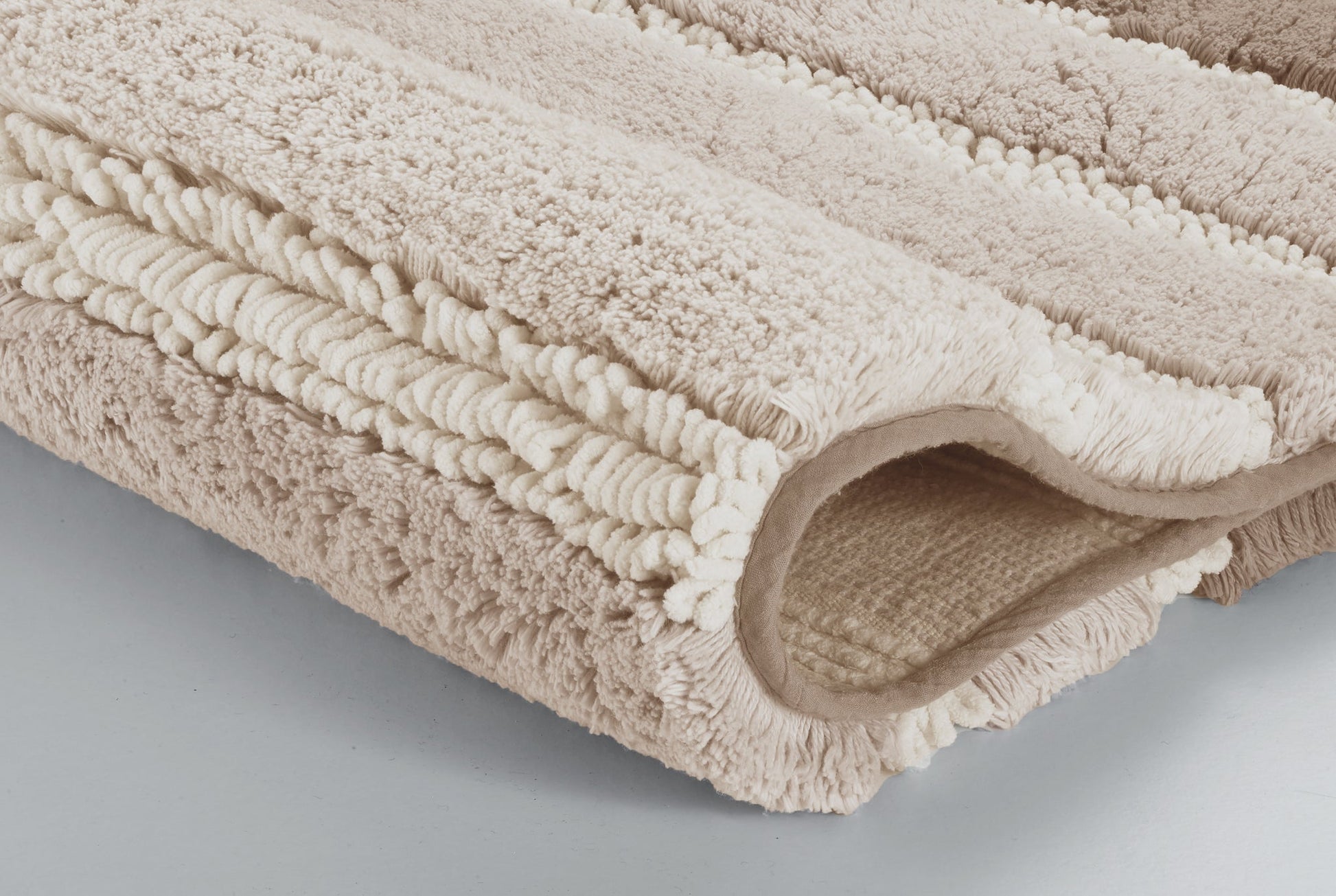 Gefaltete, beige Badematte mit flauschiger, strukturierter Oberfläche
