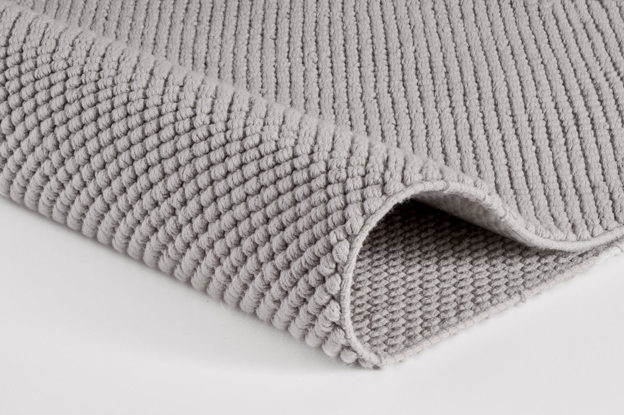 Graue, gerippte Badematte aus Textil in Nahaufnahme auf weißem Untergrund