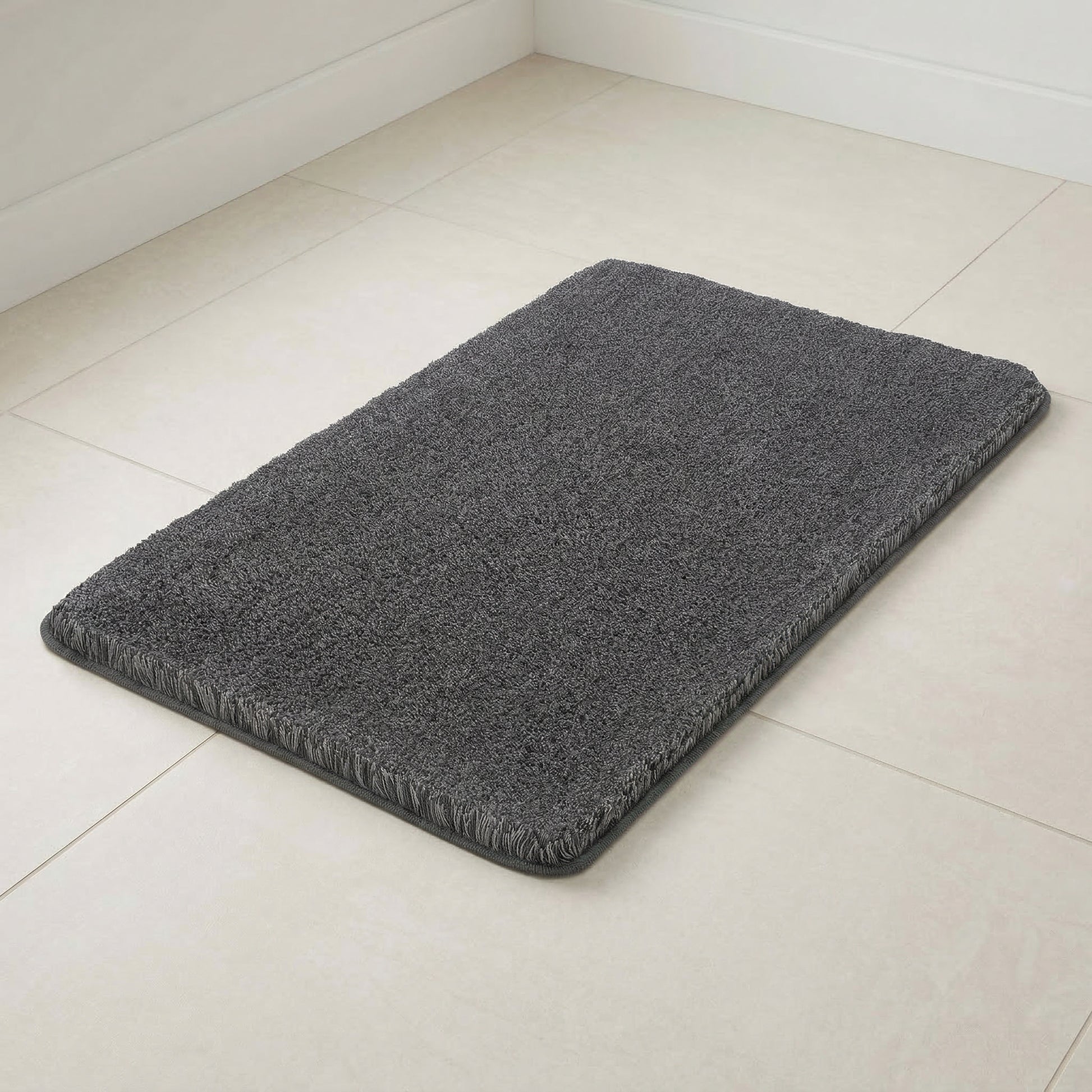 Grauer Badteppich auf hellen Badezimmerfliesen in Zimmerecke.