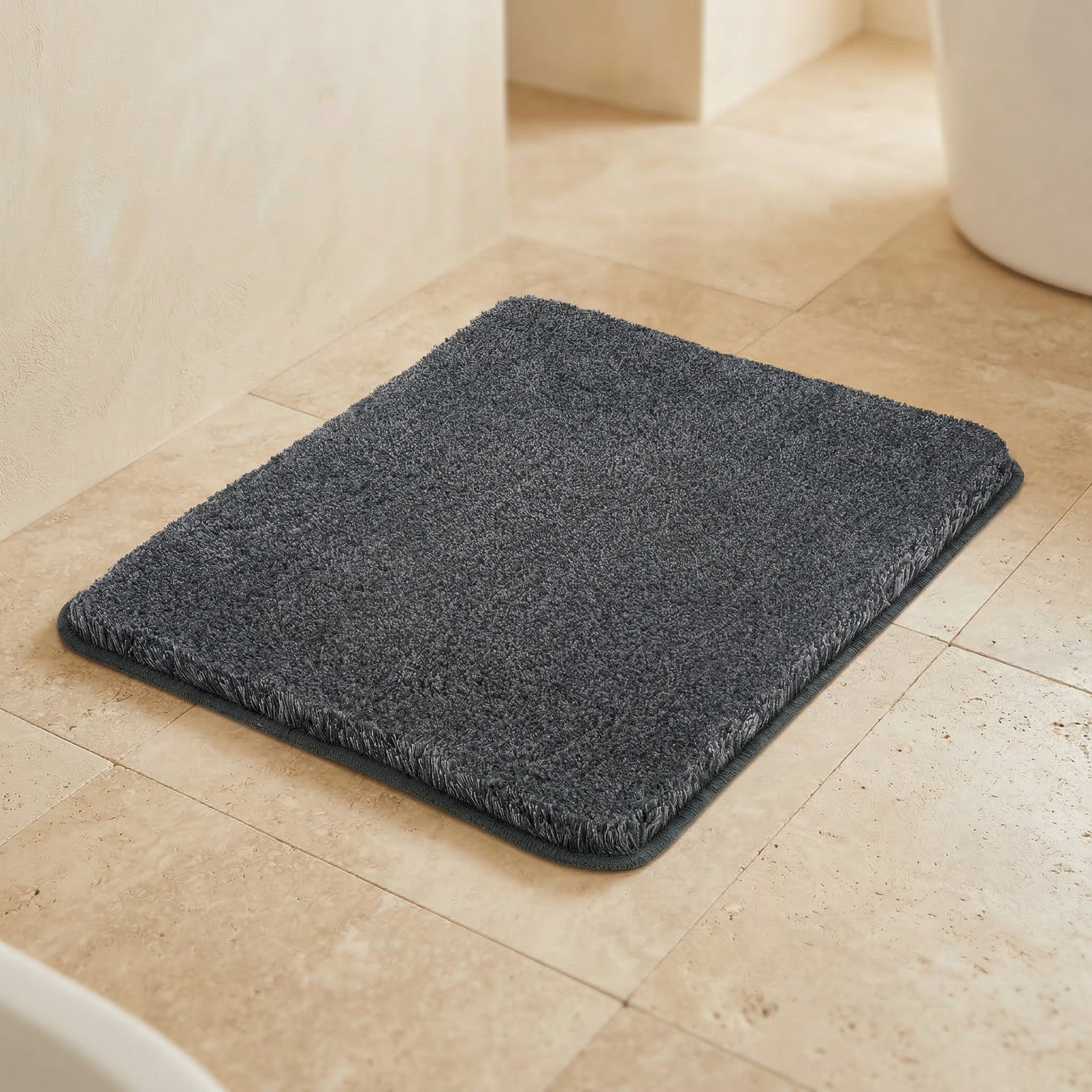 Dunkelgrauer Badteppich auf beigen Fliesen im hellen Badezimmer.