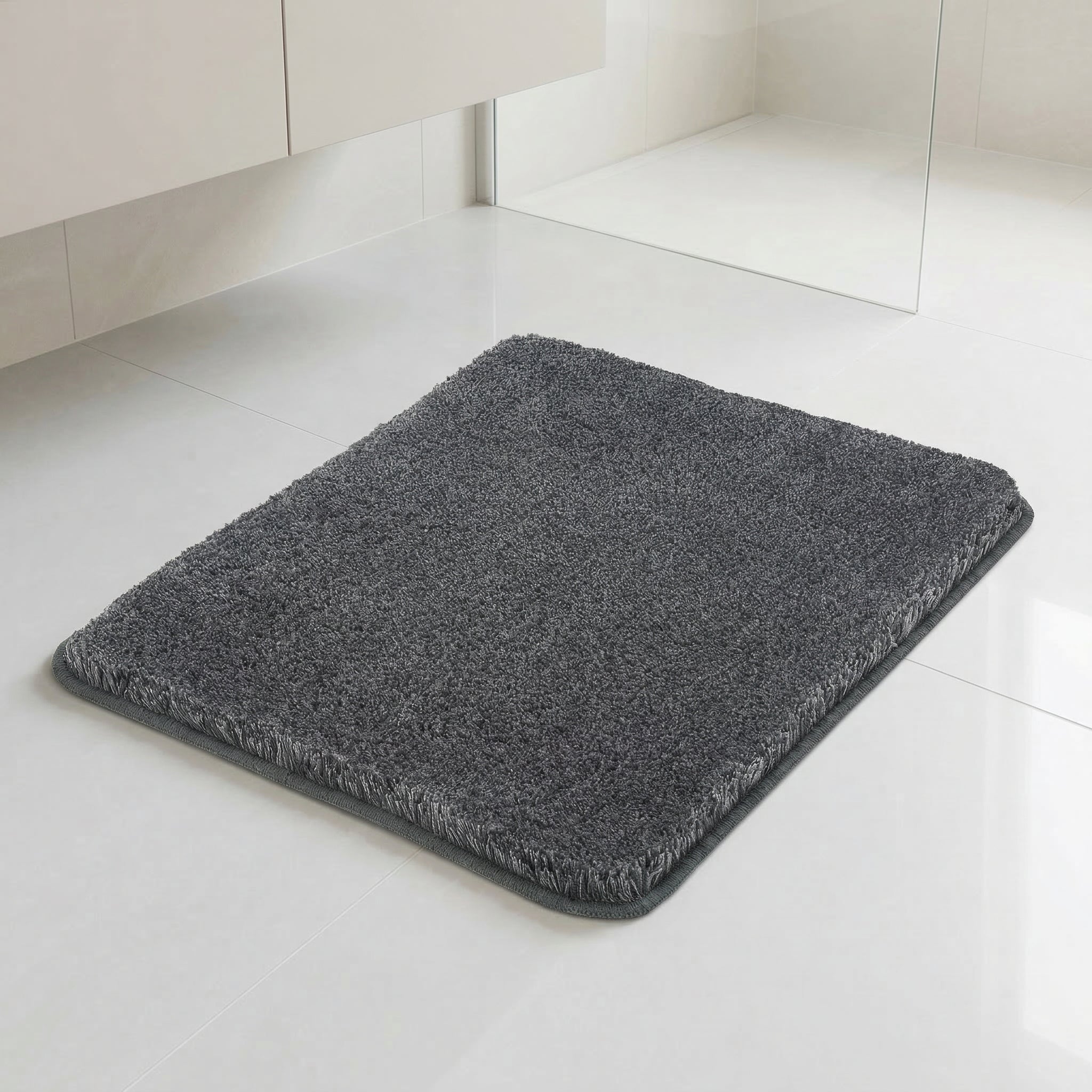 Dunkelgrauer Badteppich auf hellen Fliesen im modernen Badezimmer.