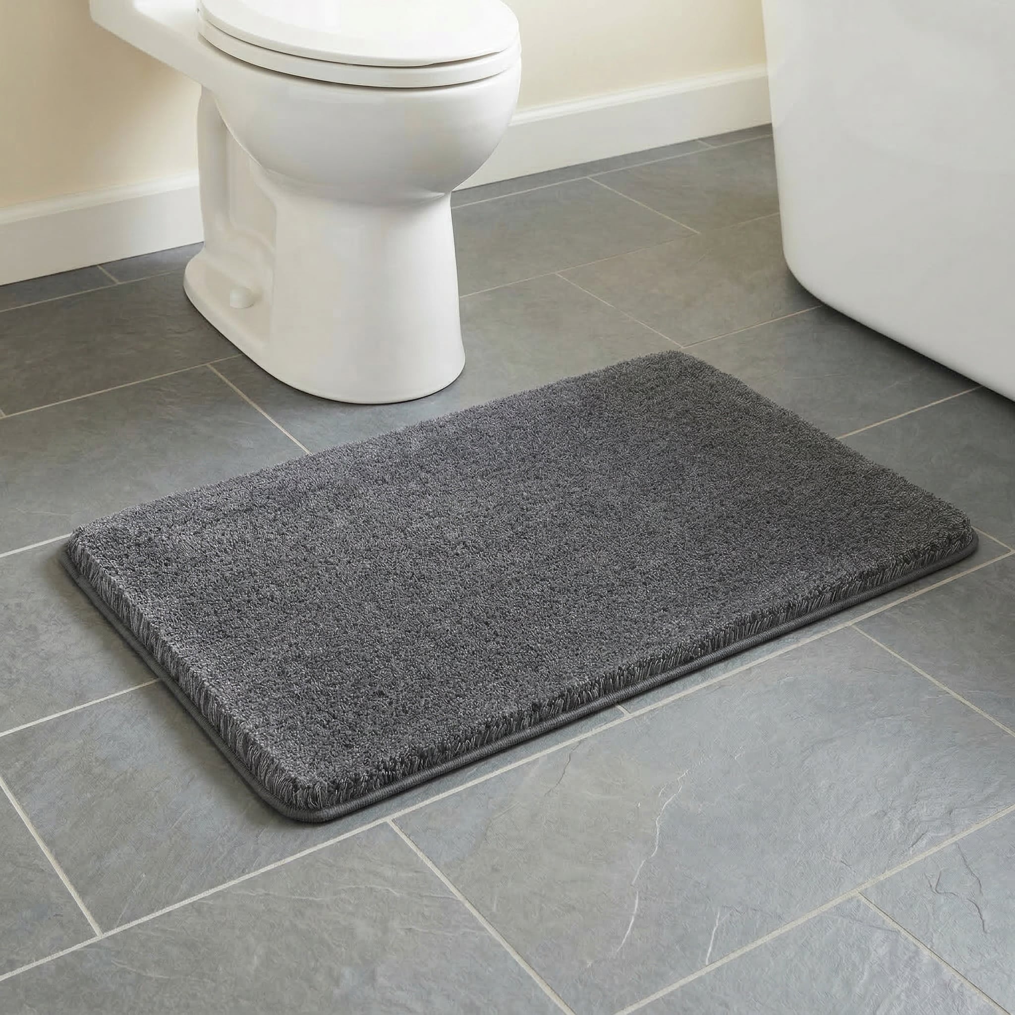 Grauer Badteppich auf Fliesenboden im Badezimmer neben Toilette und Wanne