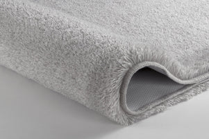 Nahaufnahme einer grauen, flauschigen Badematte mit umgeschlagener Ecke