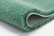 Nahaufnahme eines mintgrünen, flauschigen Badteppichs mit gefalteter Kante