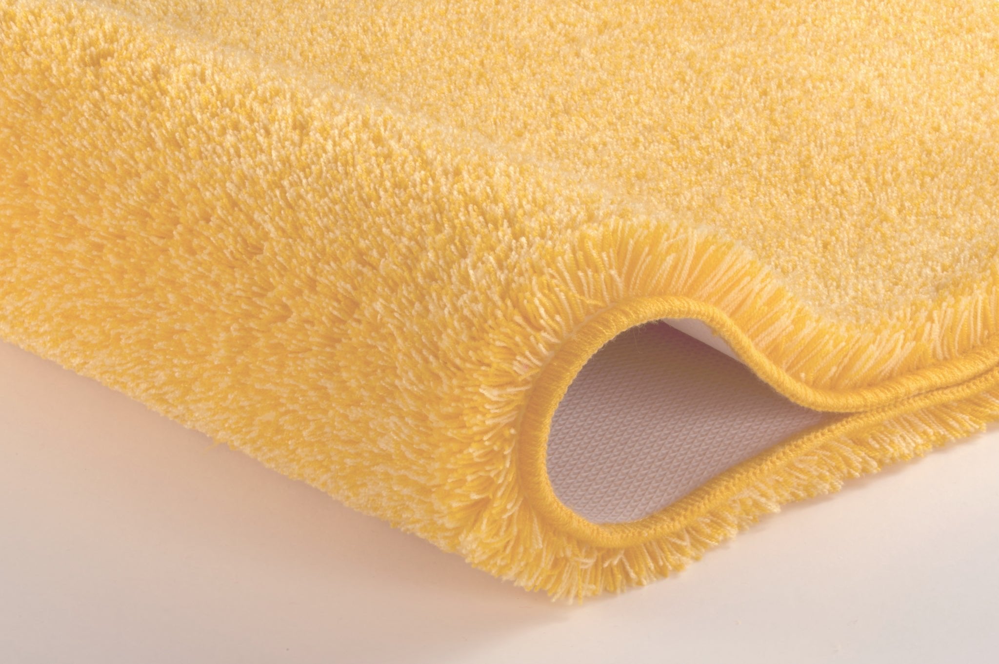 Gelber Badteppich RELAX Mimose 50 x 80 cm liegt mit hochflorigem Rand auf hellem Boden.